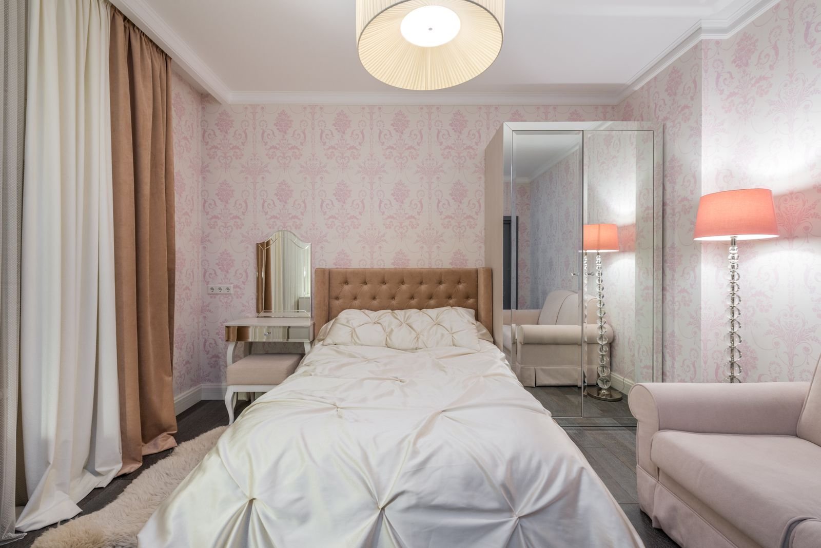 Pink-walled bedroom with a bed, sofa, lamps and curtains.
