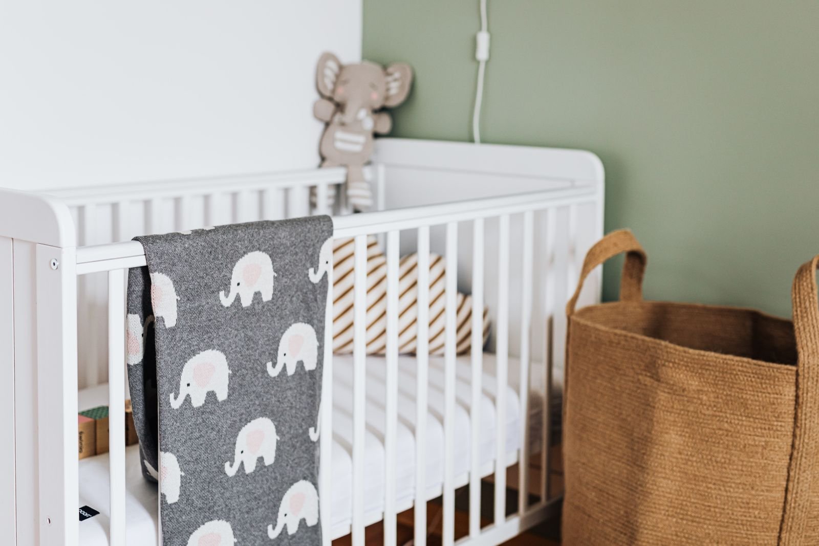 White wooden crib with a soft elephant blanket hanging on it.