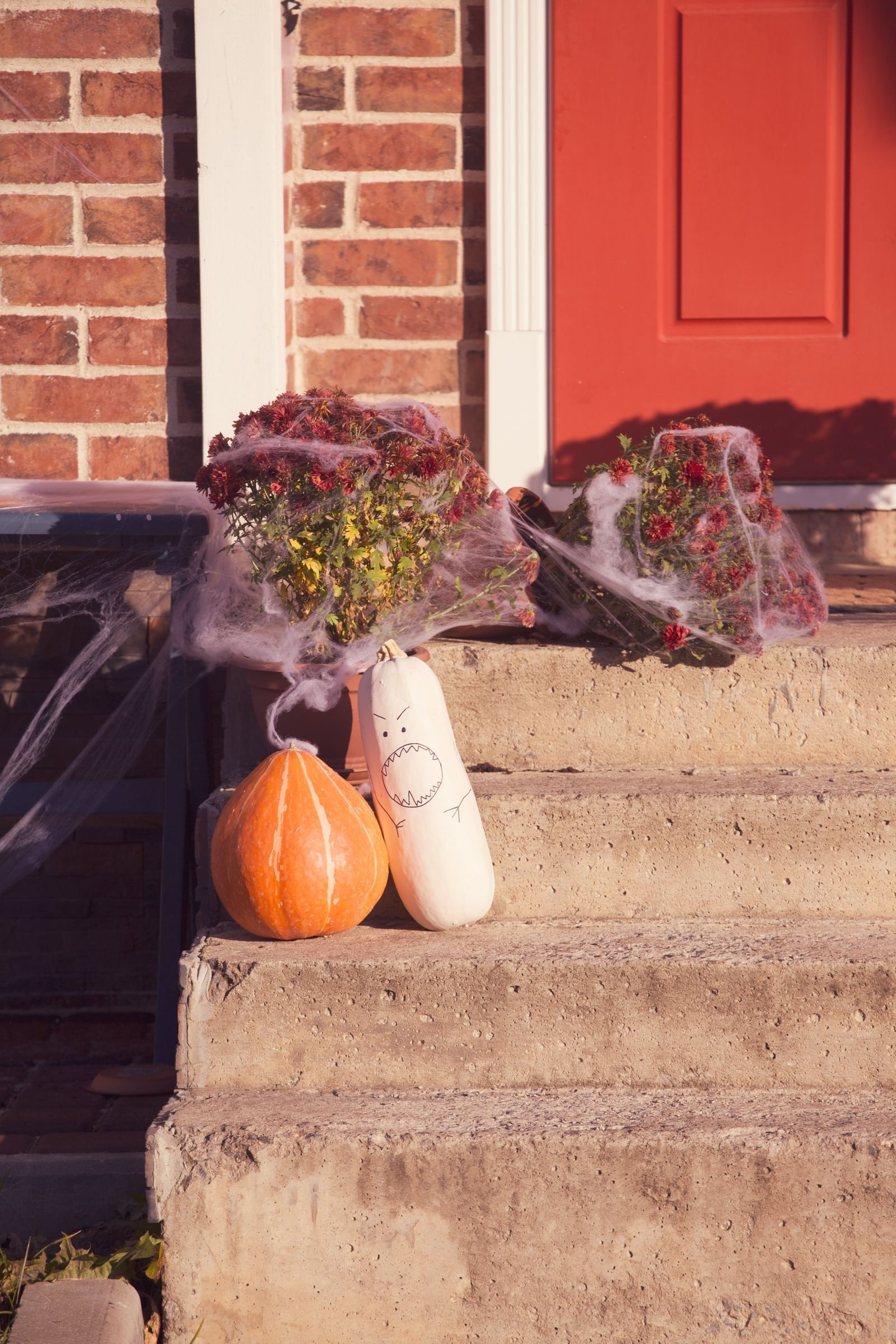 Pumpkins and spider webs decorating a brick porch with a red door