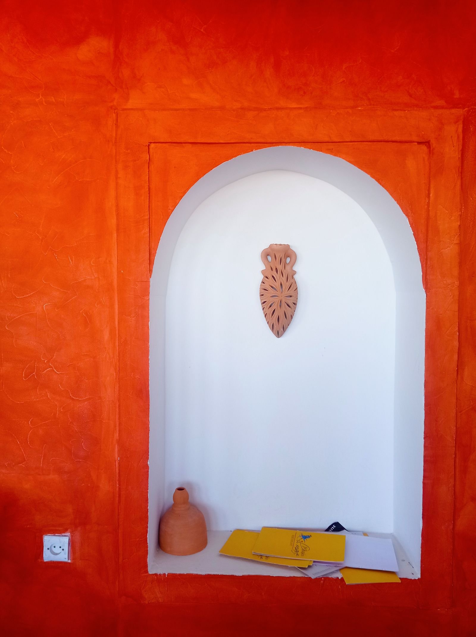 Terracotta-orange wall with a white niche holding pottery and decor.