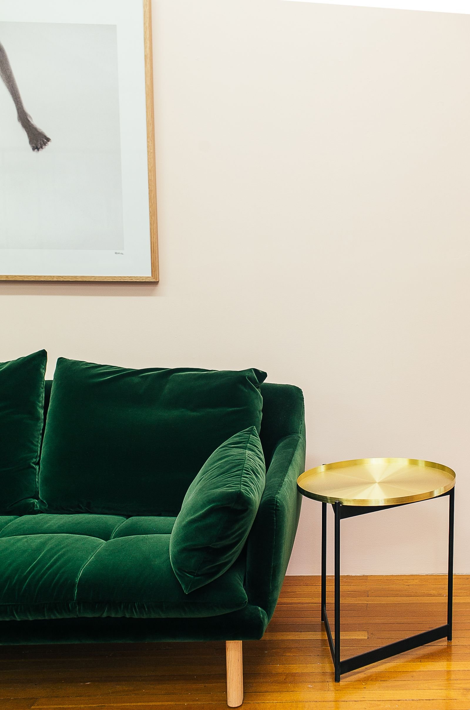 Green velour couch with cushions beside a small round table.