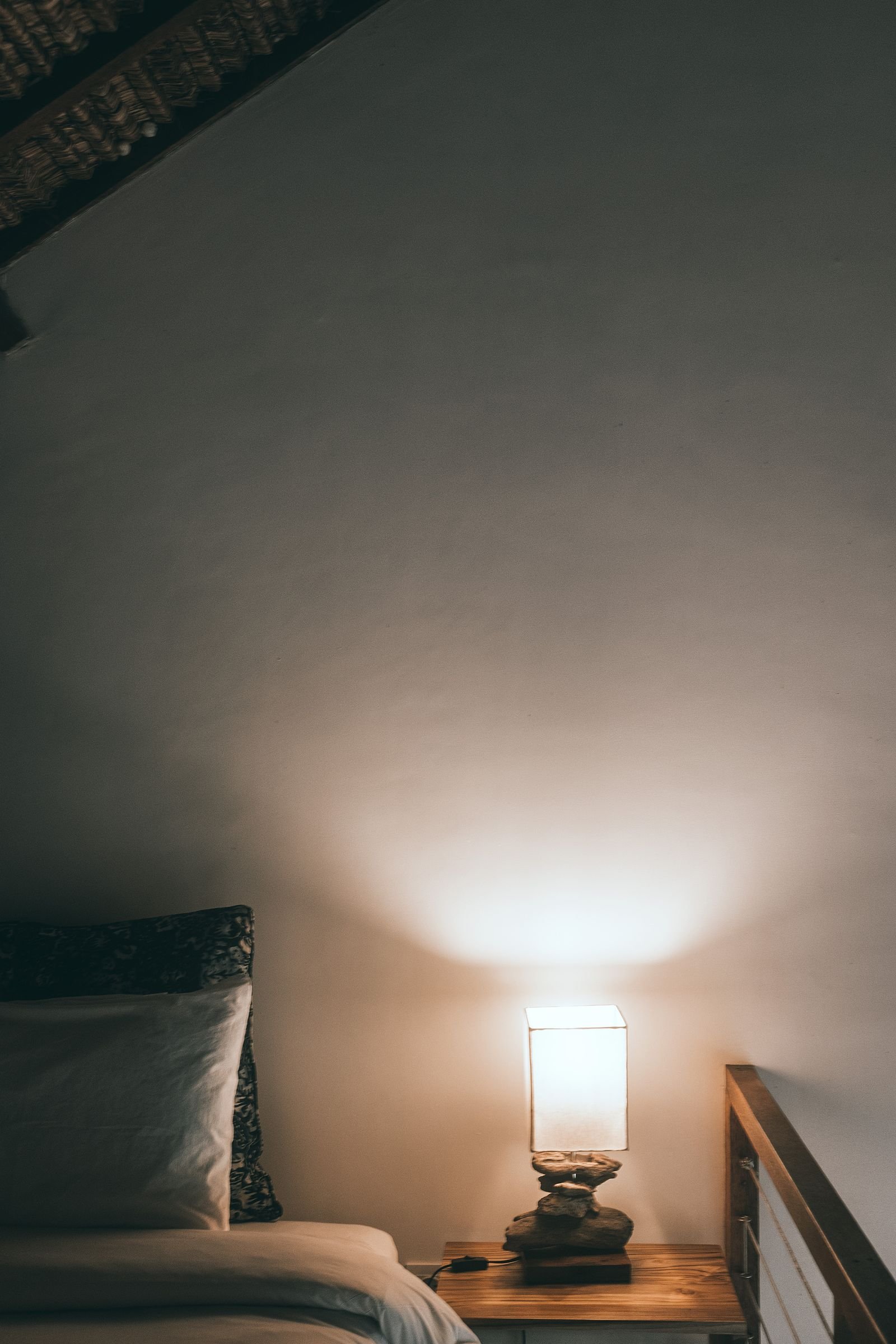 Lit bedside lamp beside soft pillows in a cozy bedroom.