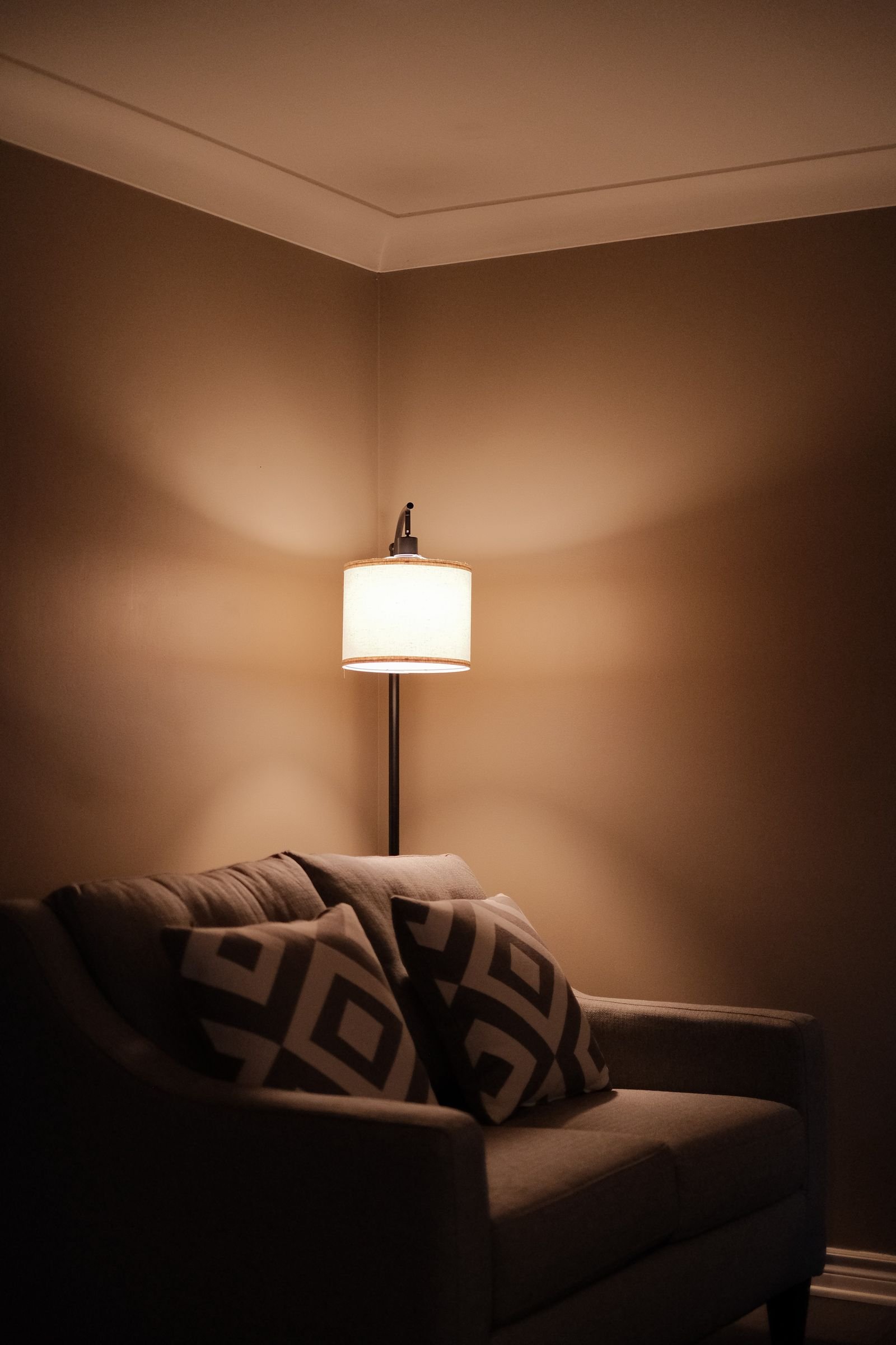 Sofa with decorative pillows beside a softly glowing lamp in a living room corner.