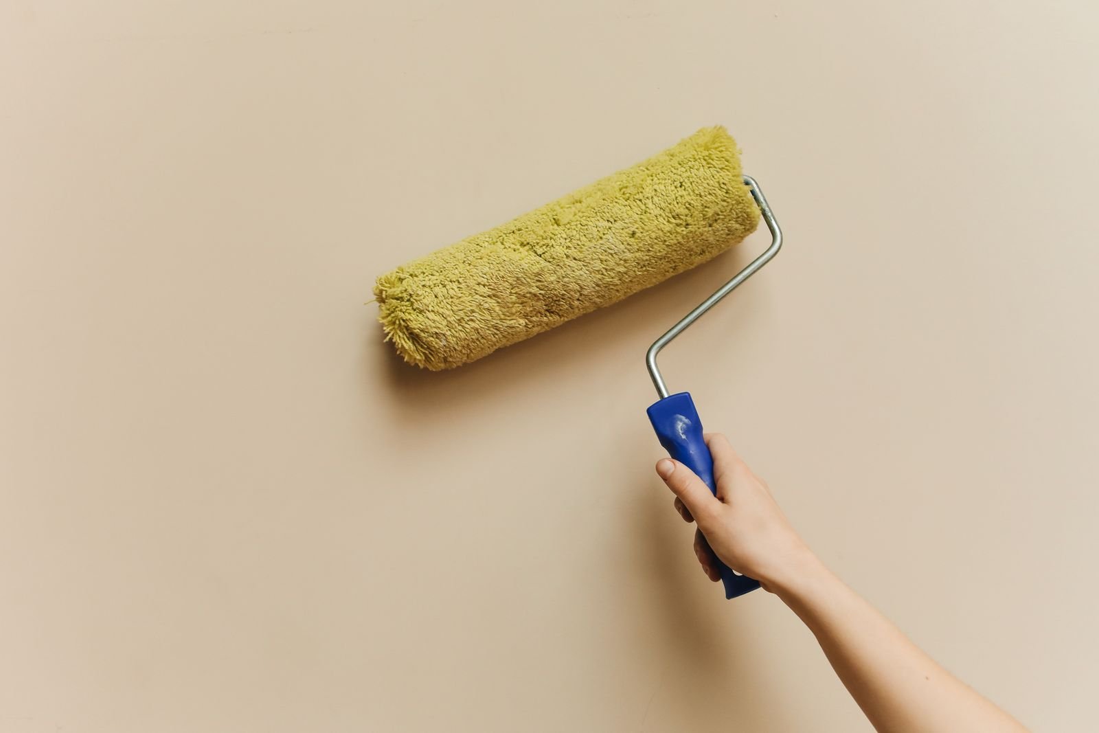 Hand rolling yellow paint onto a beige wall.
