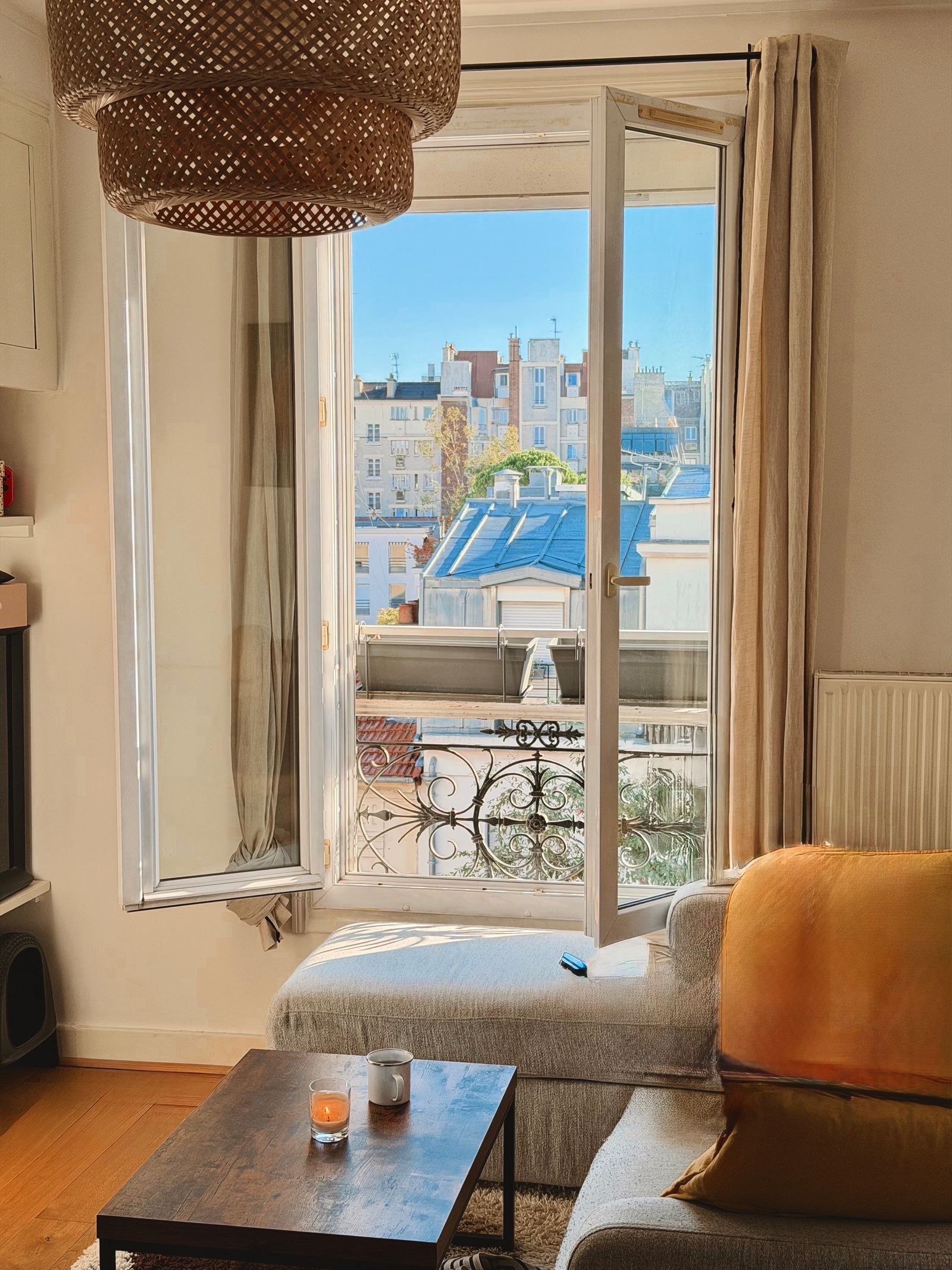 Bright, cozy living room with an open window overlooking rooftops.