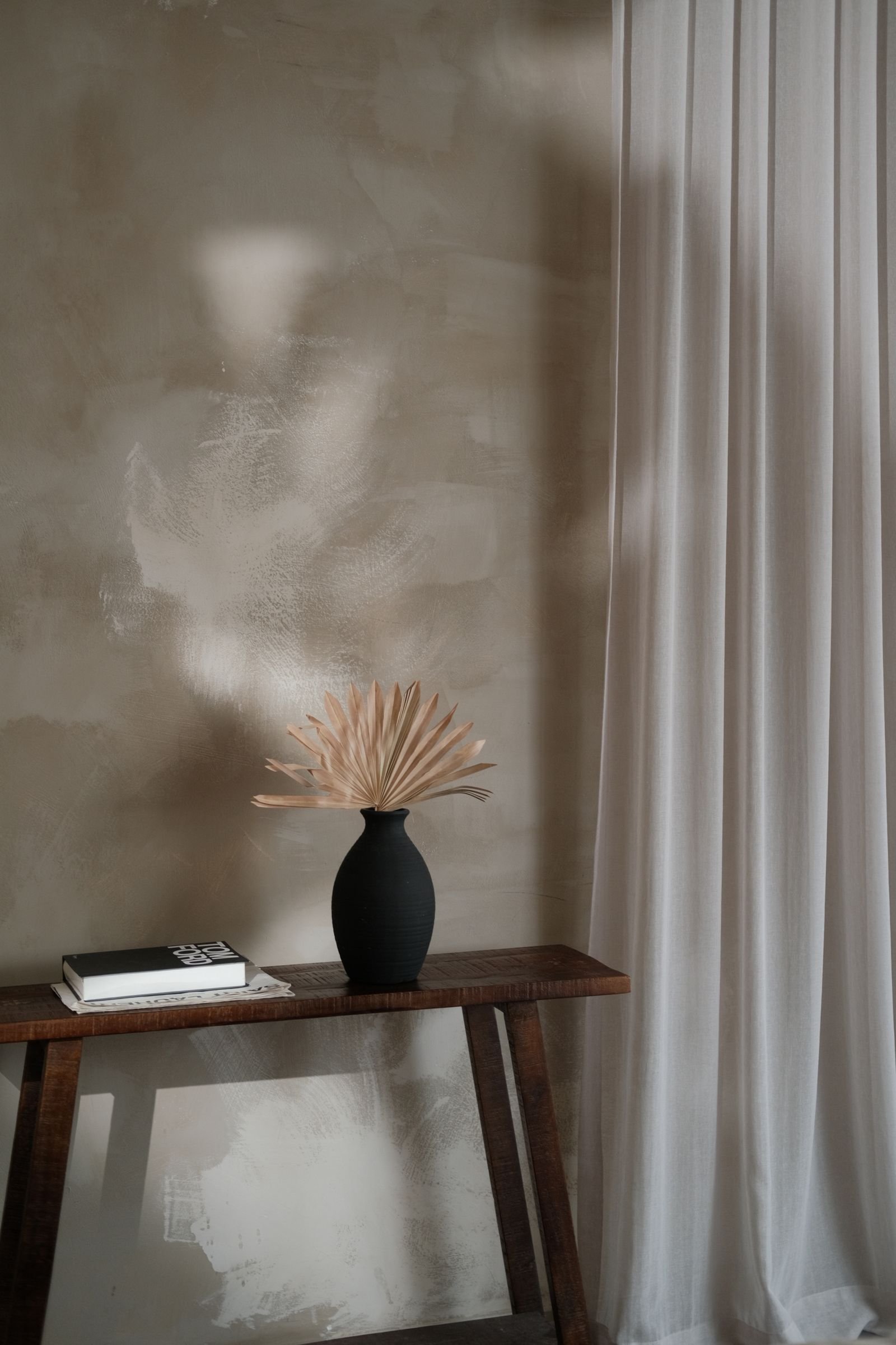 Black vase with dried flowers on a console table by a textured wall.