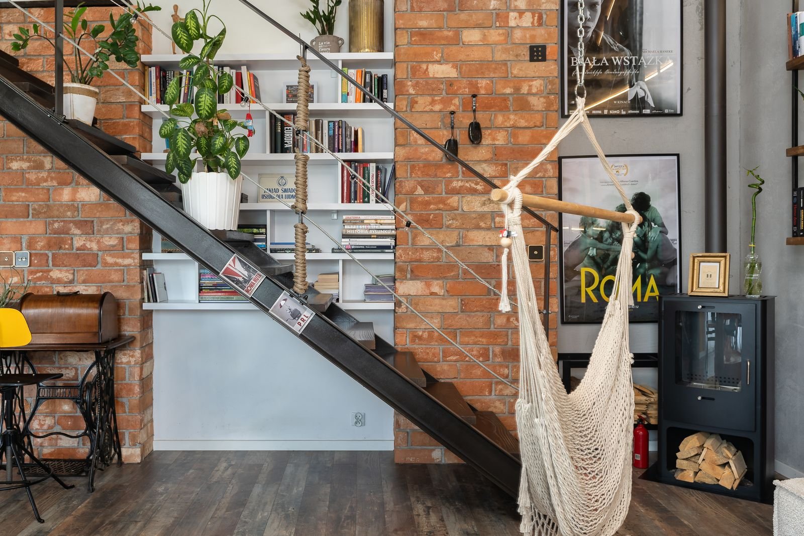 Industrial loft with a brick wall, bookshelf, staircase and hammock.