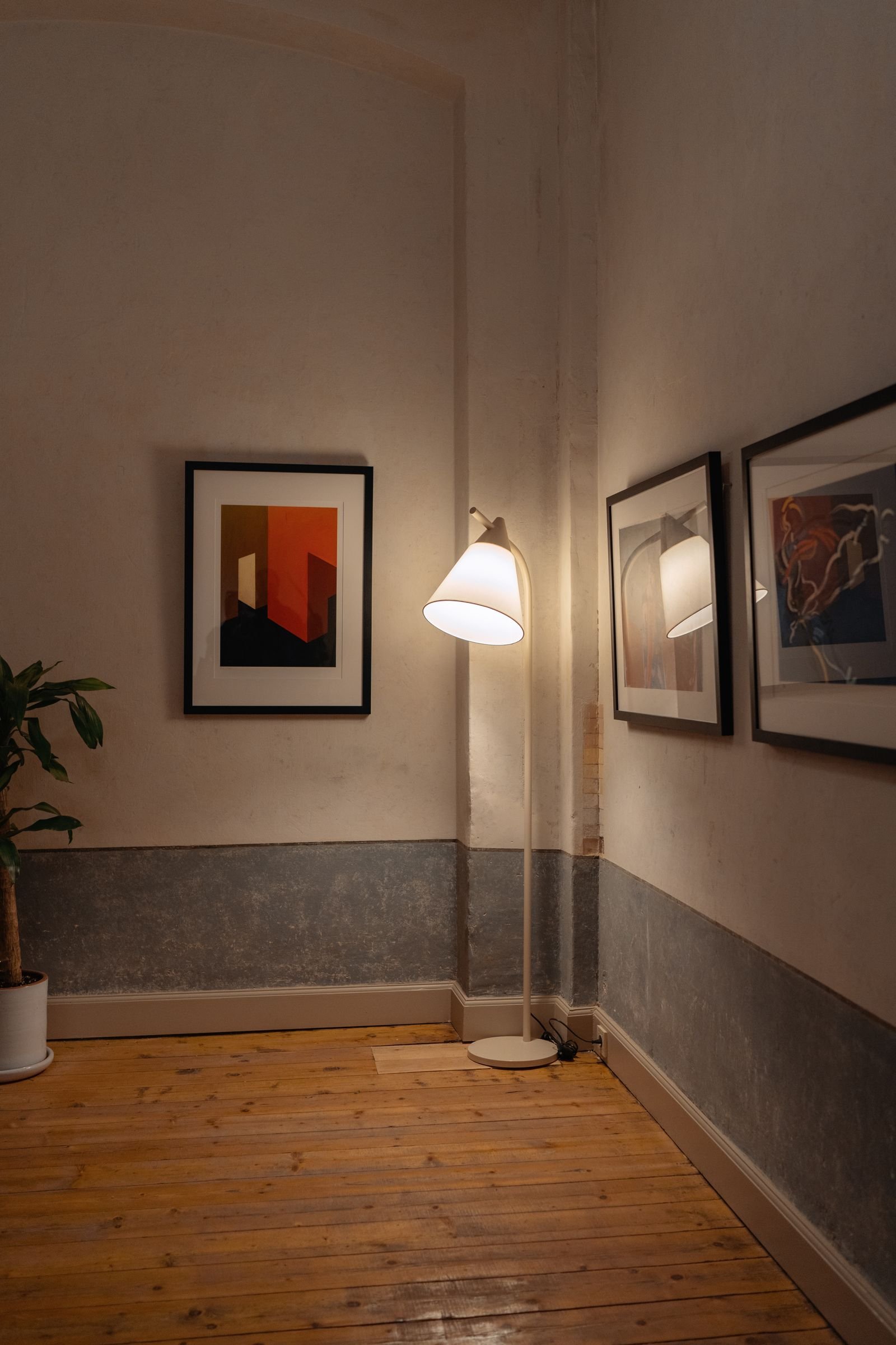 Room corner with framed art on the walls and a glowing floor lamp.