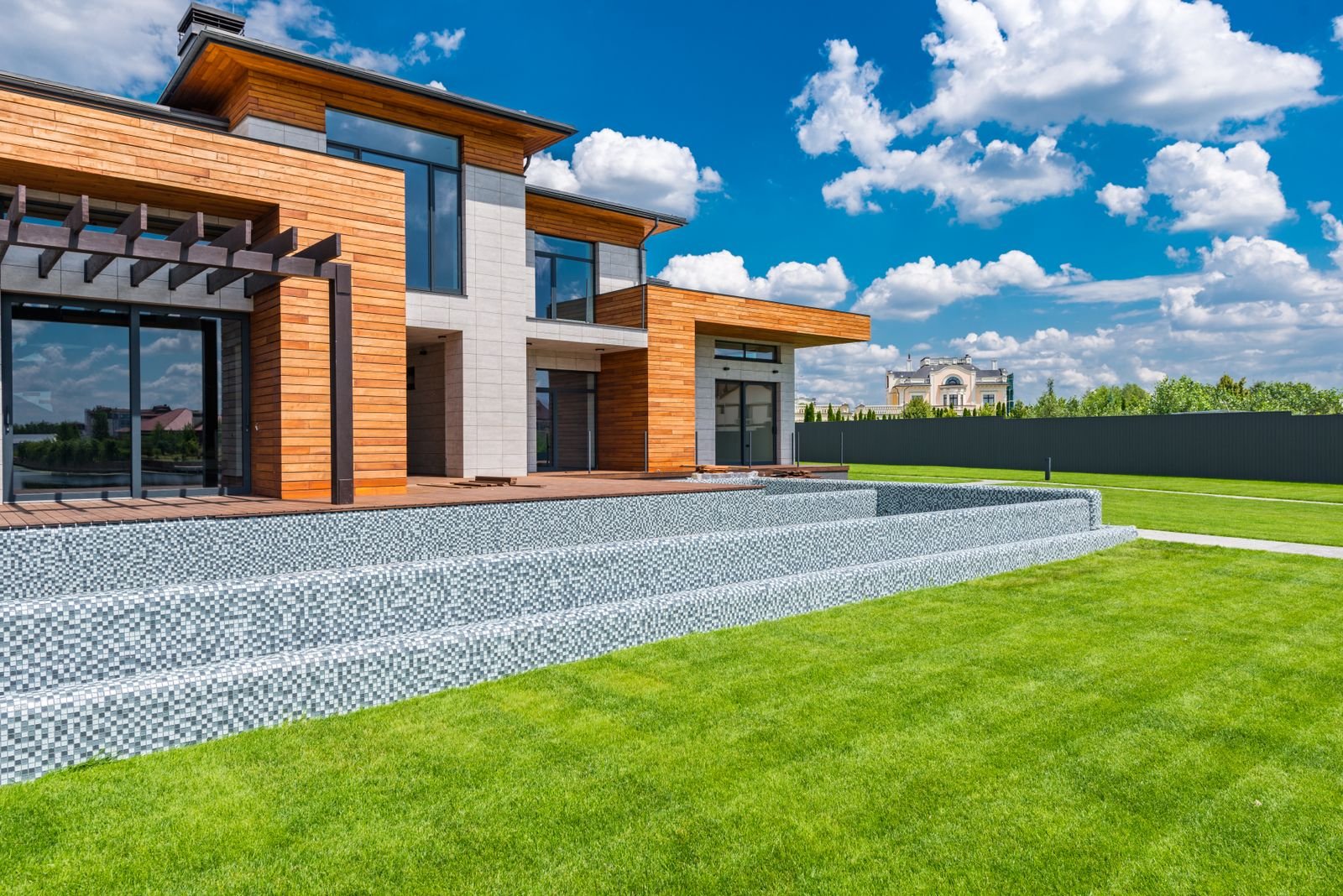 Modern house with panoramic glass doors and a green lawn on a sunny day.