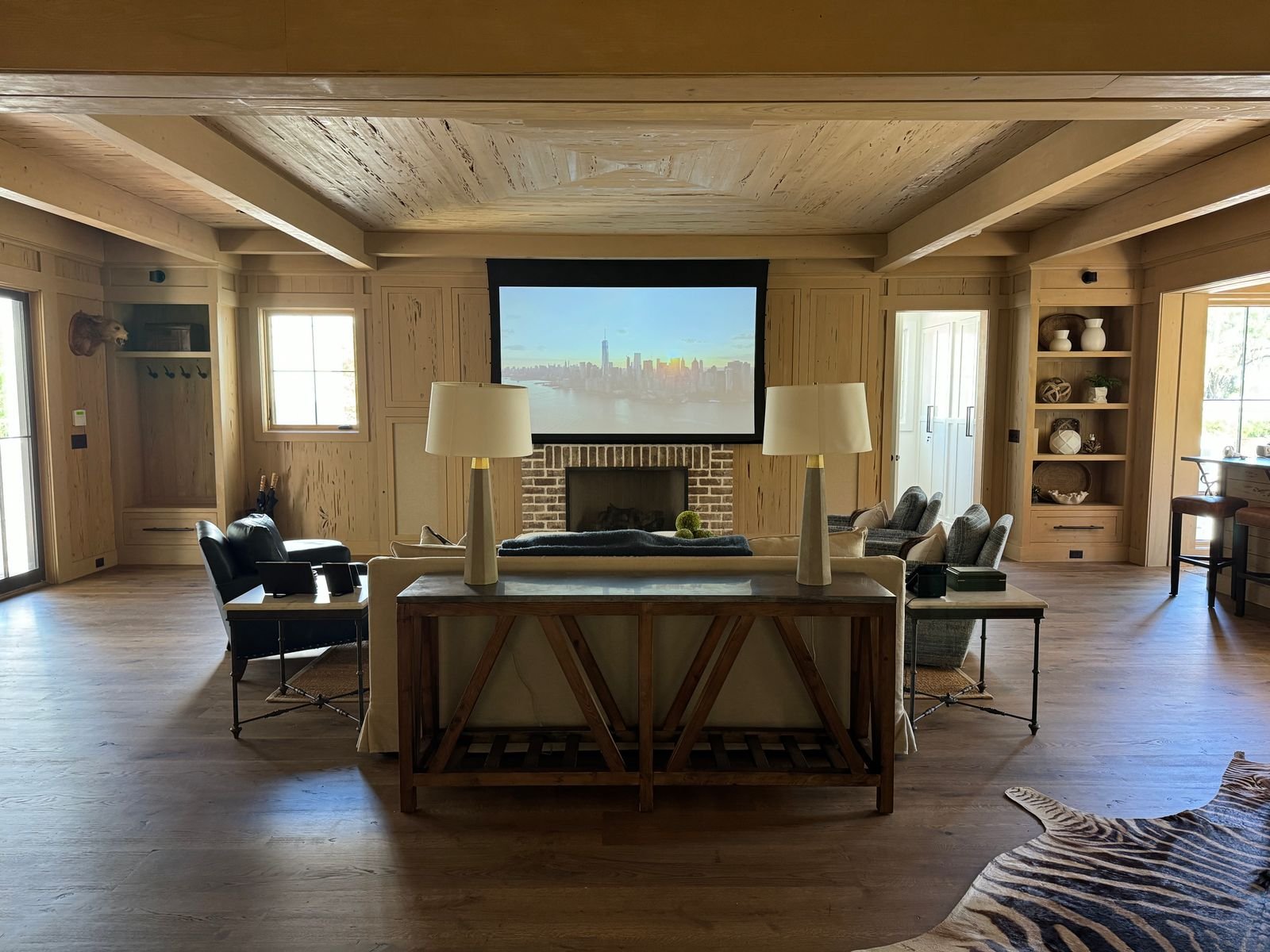 Living room with a projector screen, cozy seating and wooden decor.