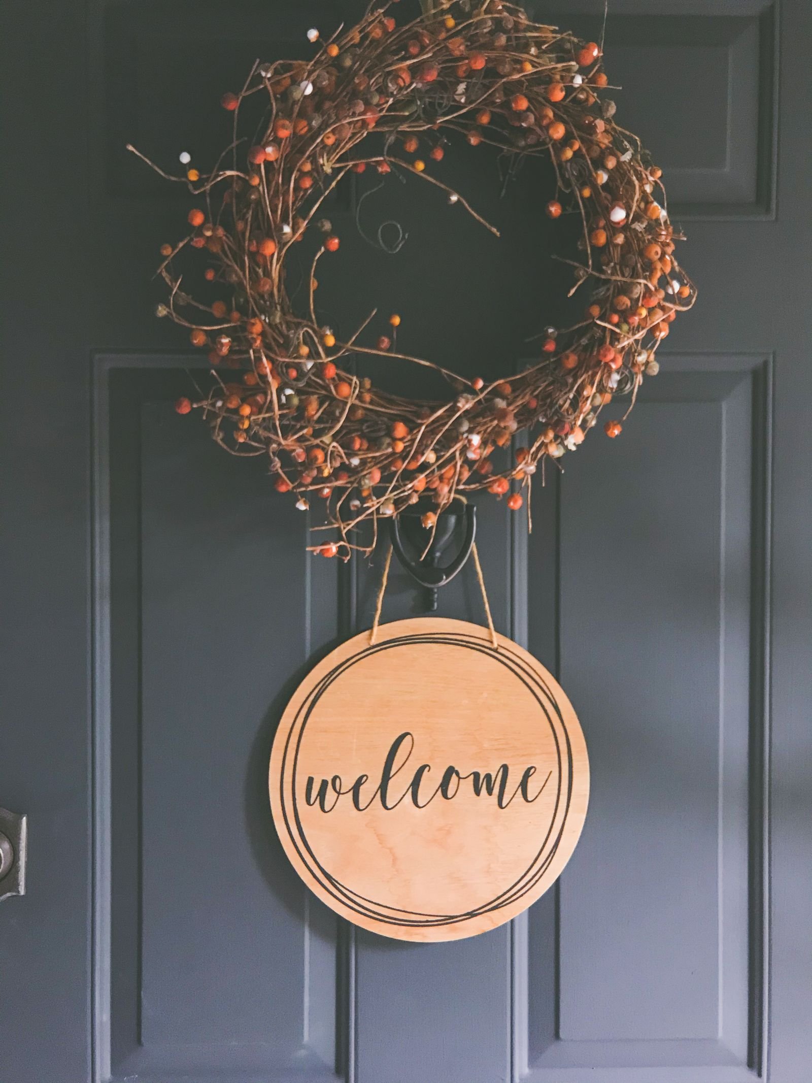 Rustic wreath and welcome sign hanging on a dark front door.