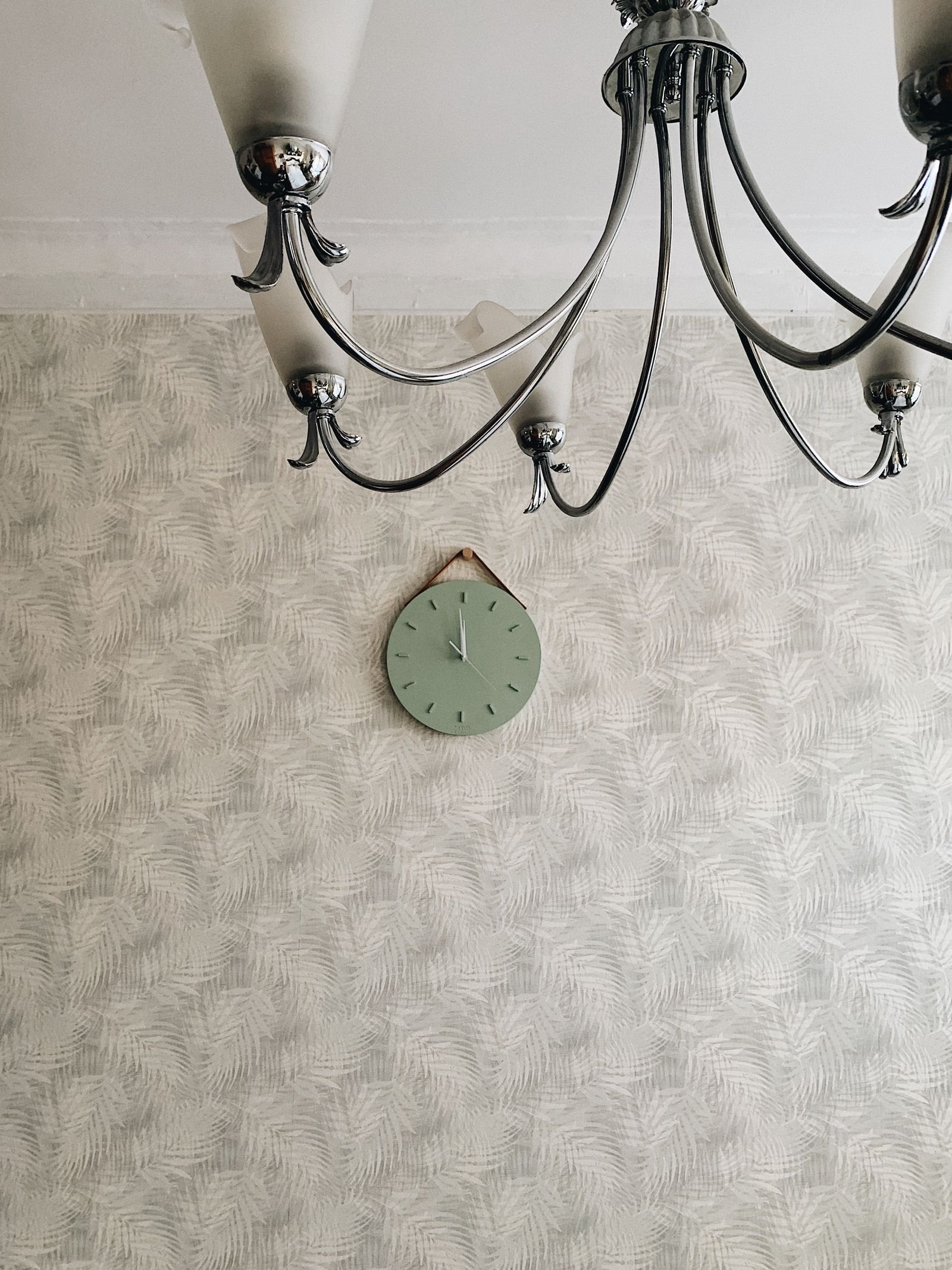 Patterned wallpaper wall with a round wall clock and a chandelier.