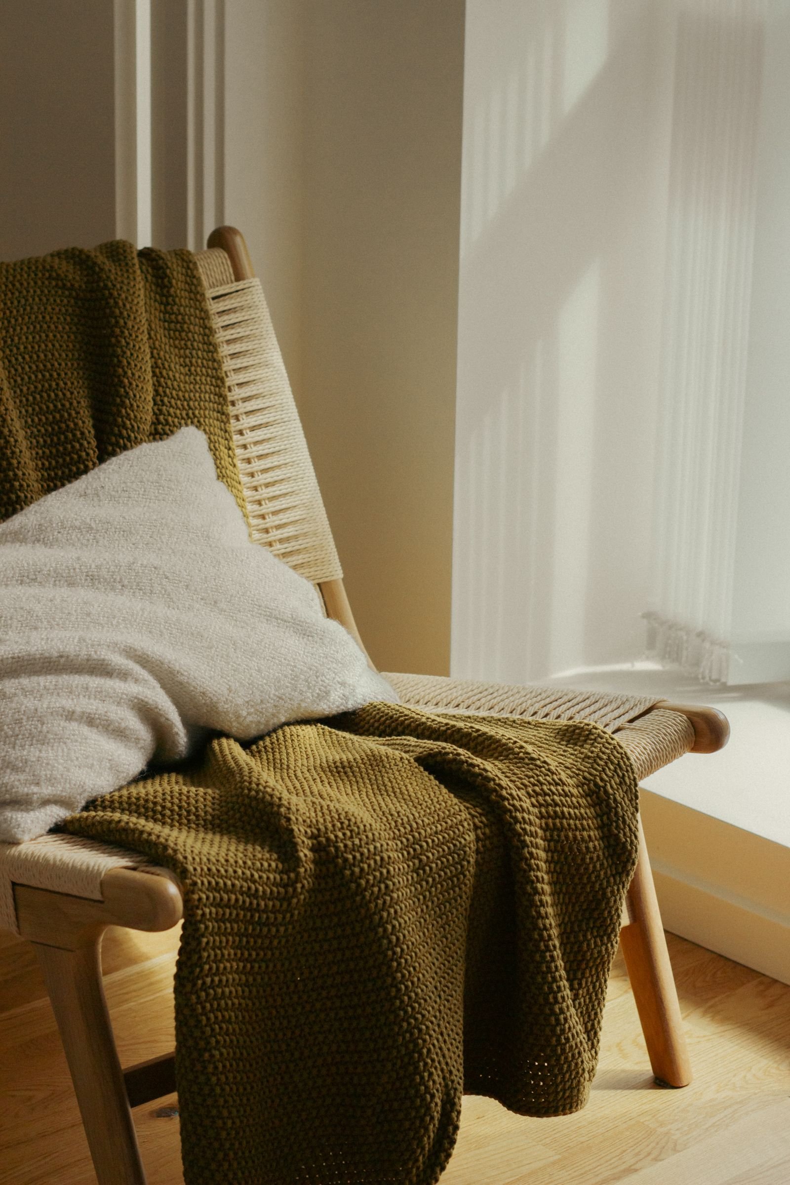 Chair with a green blanket and pillow in a sunlit room.