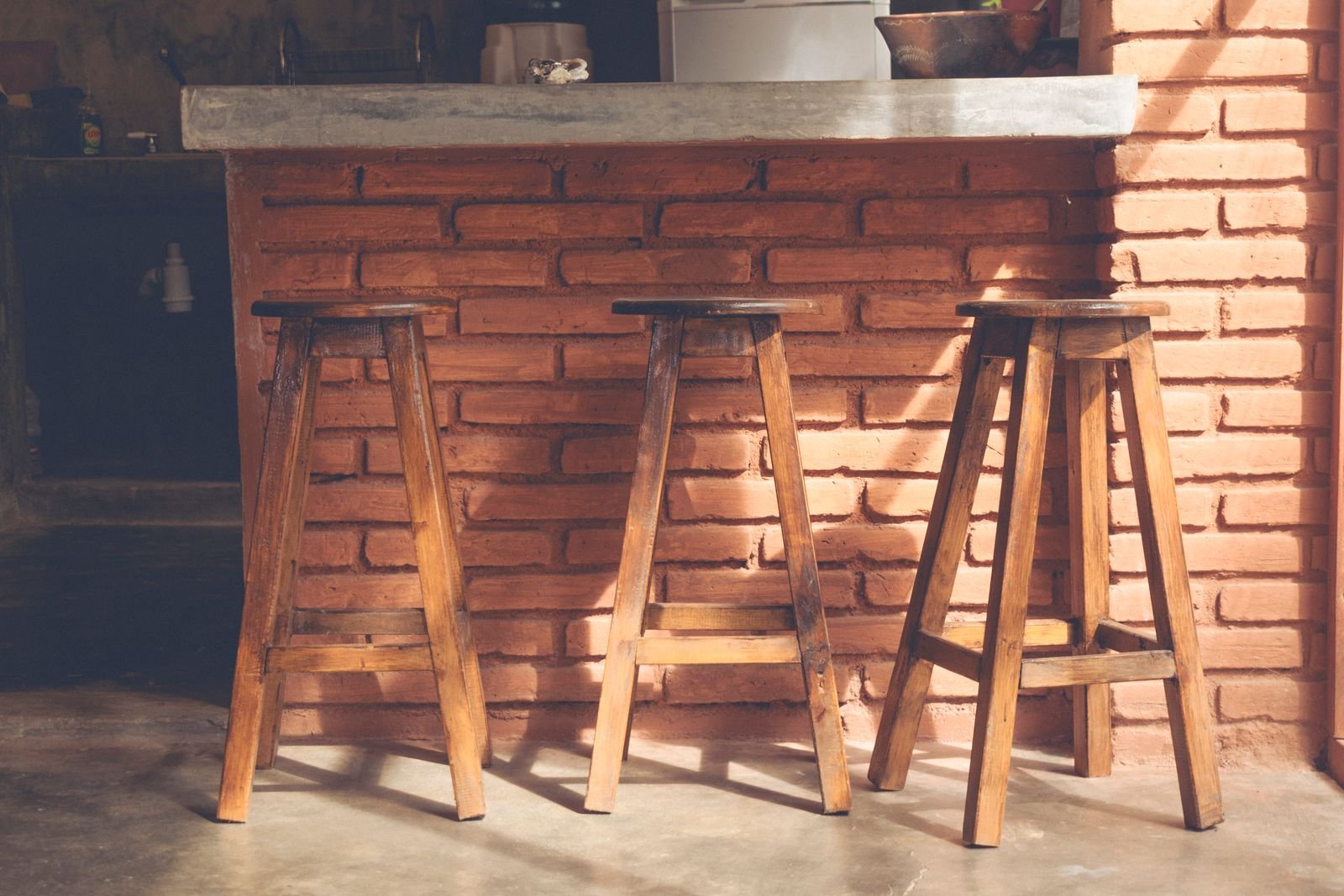 Three wooden bar stools in a rustic kitchen with brick walls.