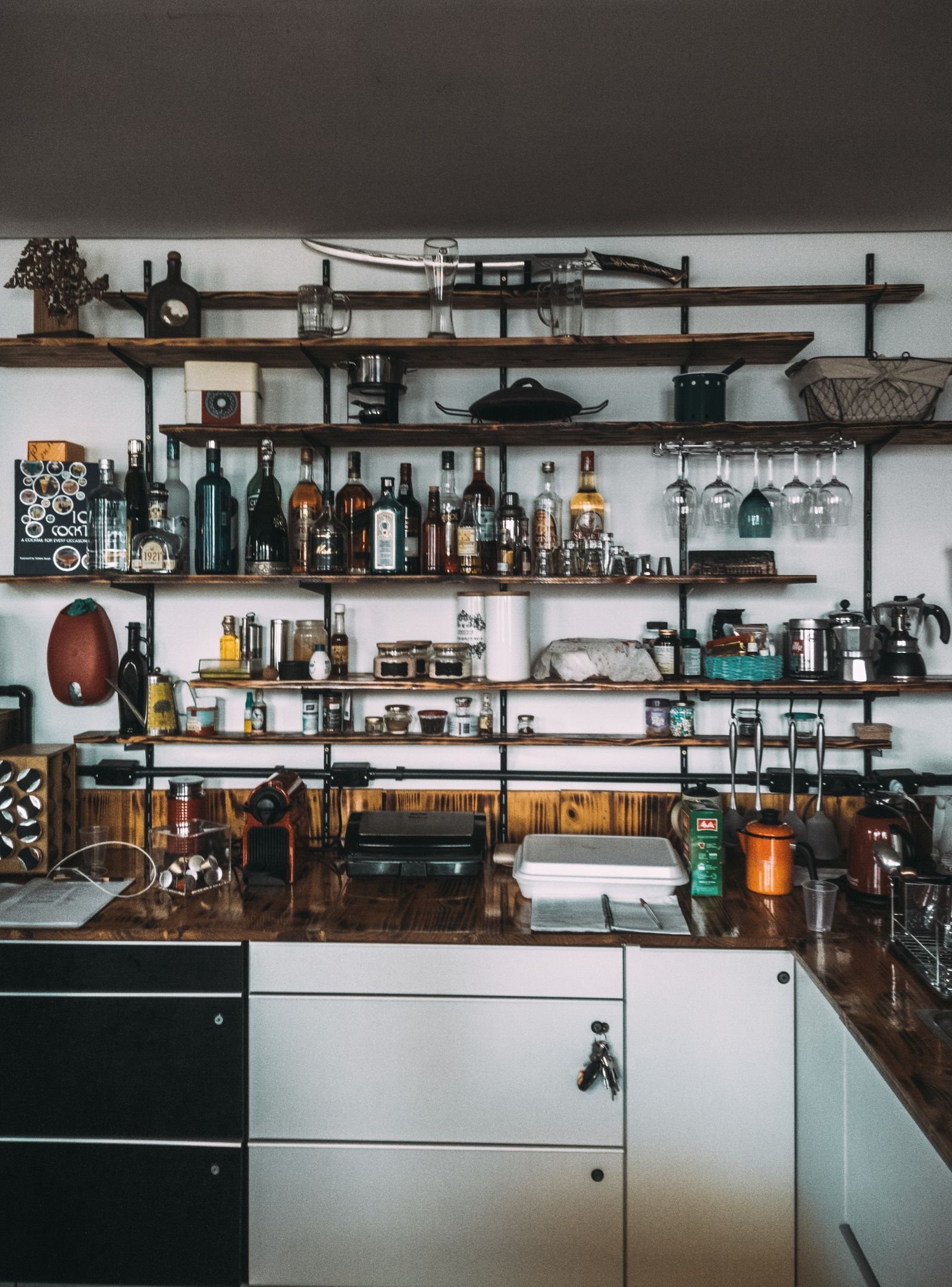 Home bar with organized bottles on wooden shelves.