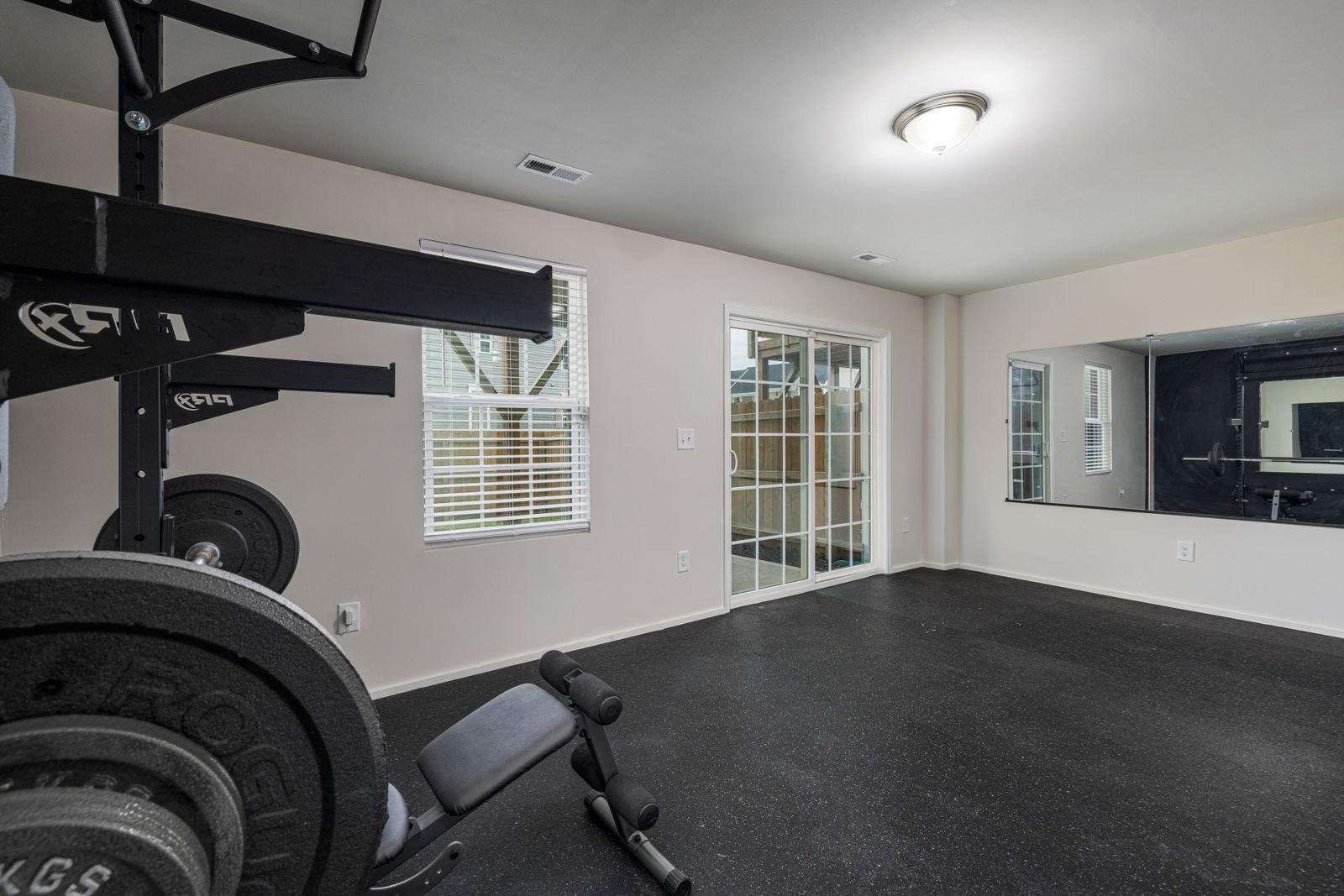 Well-lit, spacious home gym with weightlifting equipment and a large mirror.
