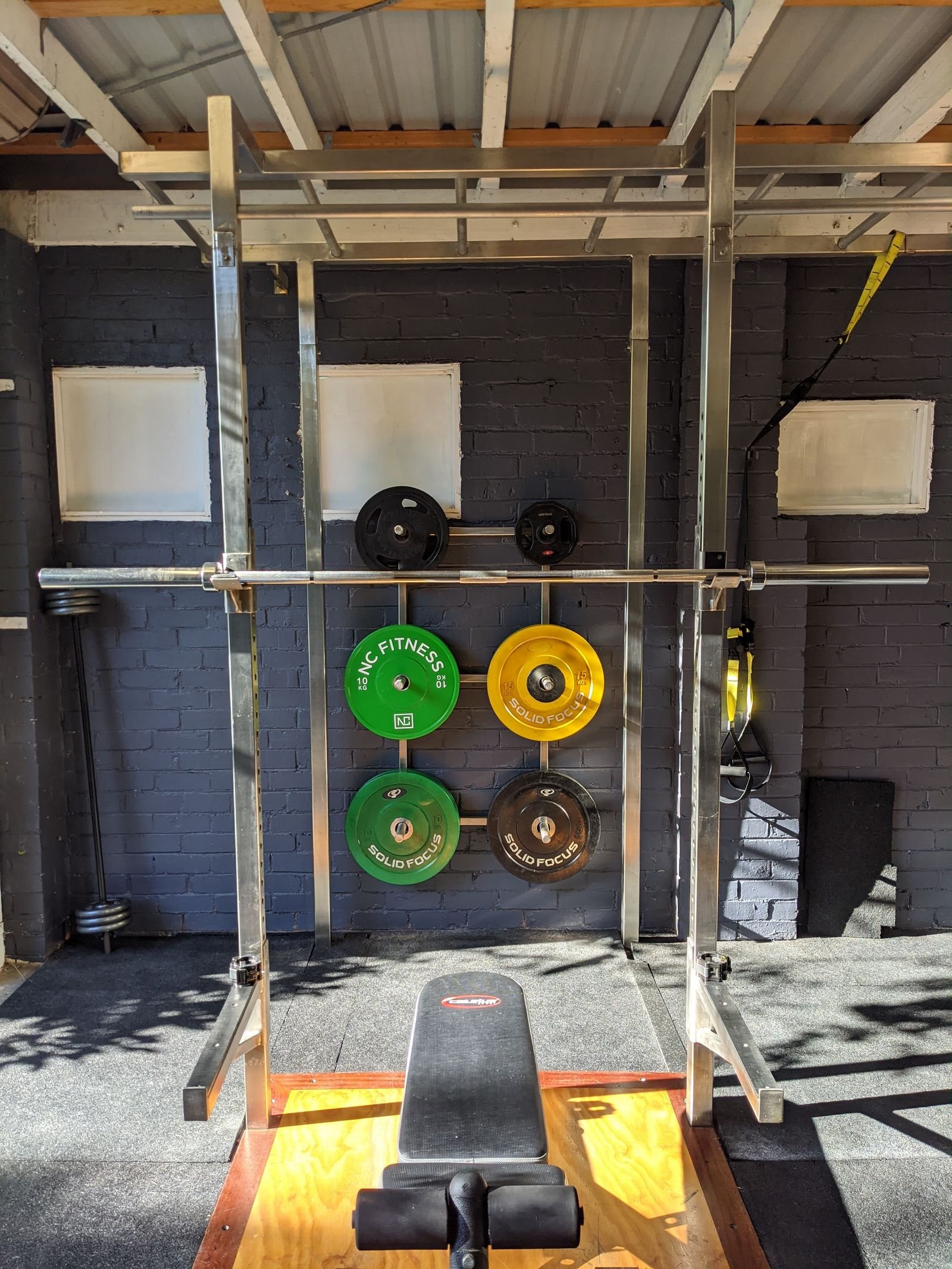 Home gym with a squat rack, weights and a bench.