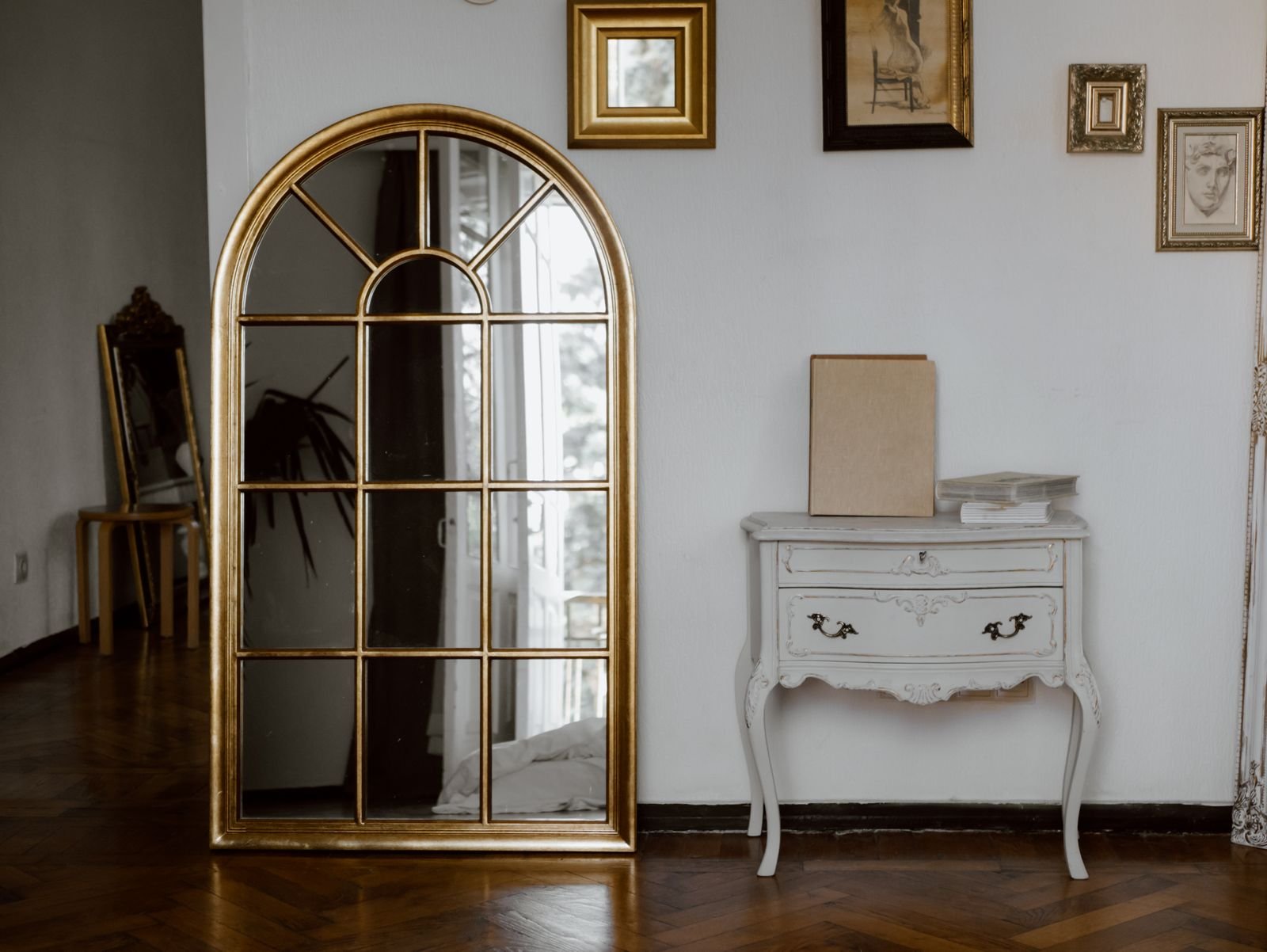Gold arched mirror above a white console table in a vintage-style room.