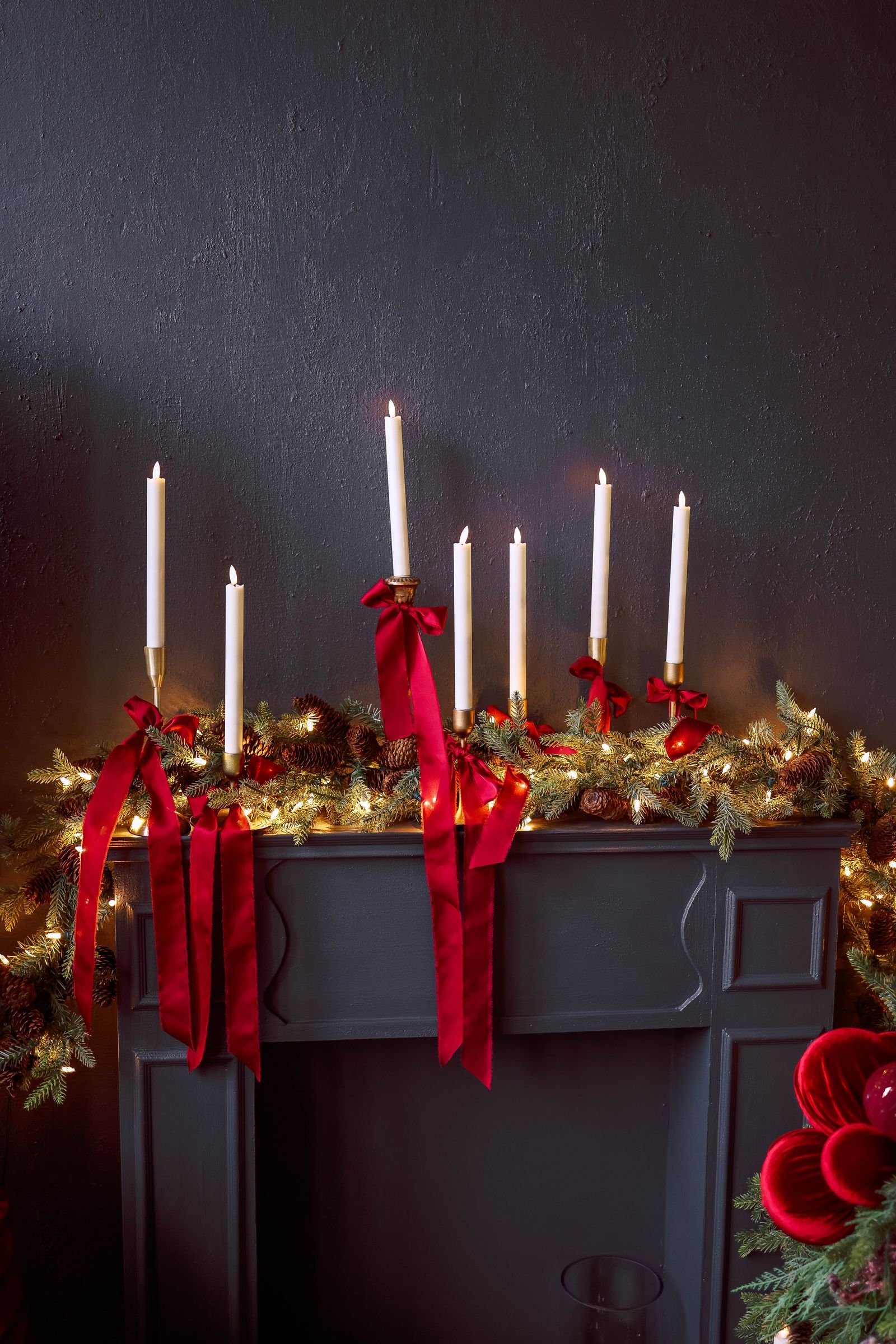 Christmas mantel decorated with candles, red ribbons and greenery.