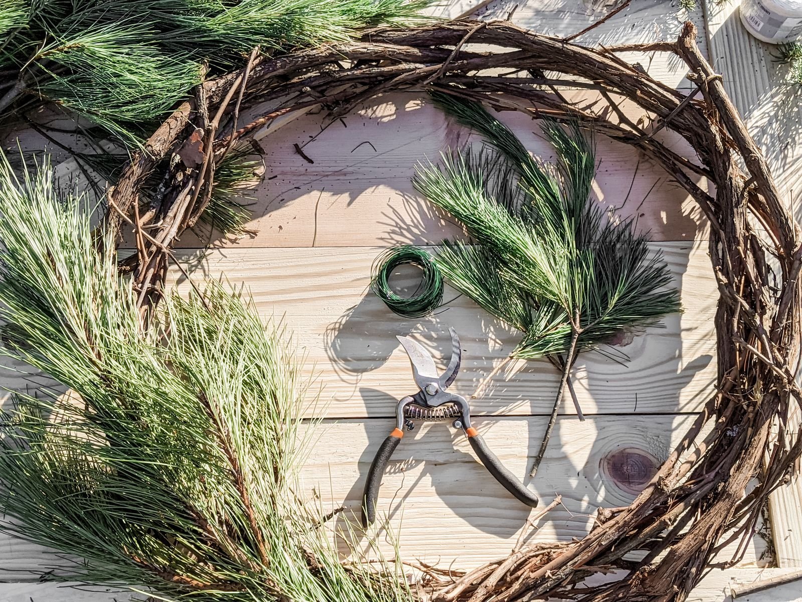 Top view of a DIY pine wreath with tools and branches on a wooden table.