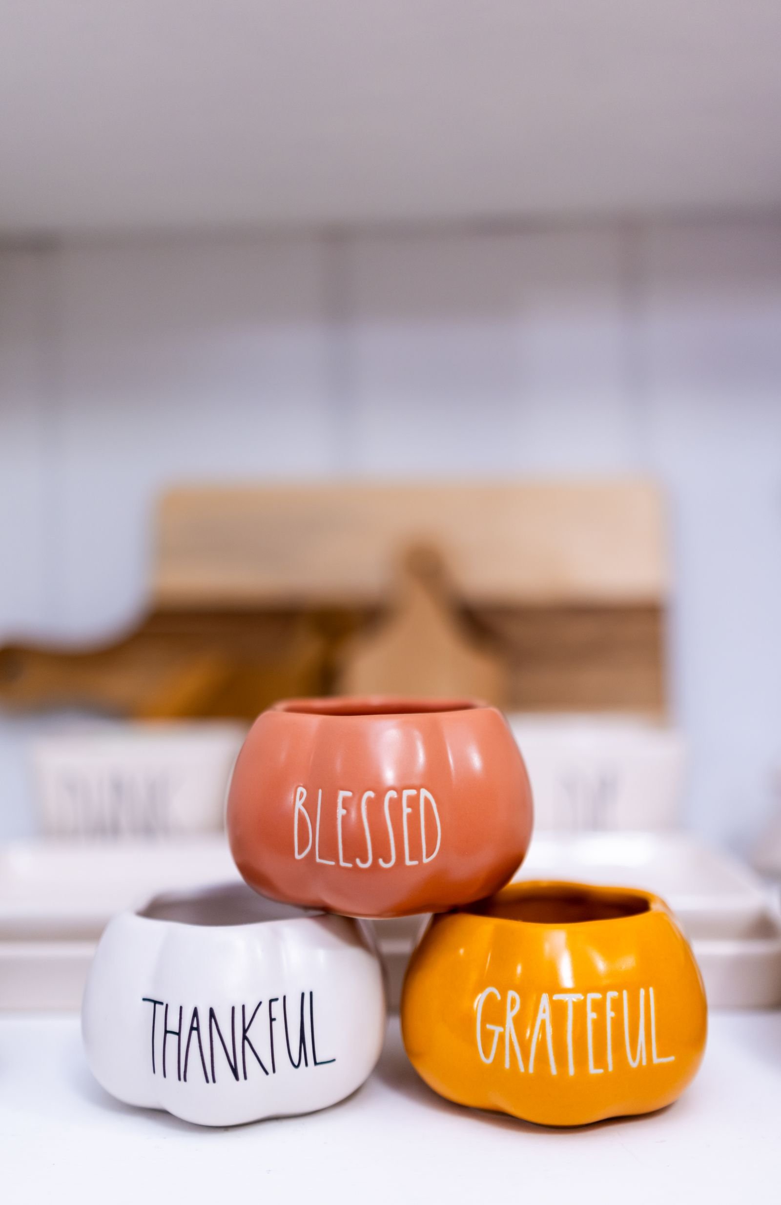 Three pottery pumpkins lettered Blessed, Thankful and Grateful, set out as Thanksgiving decor.