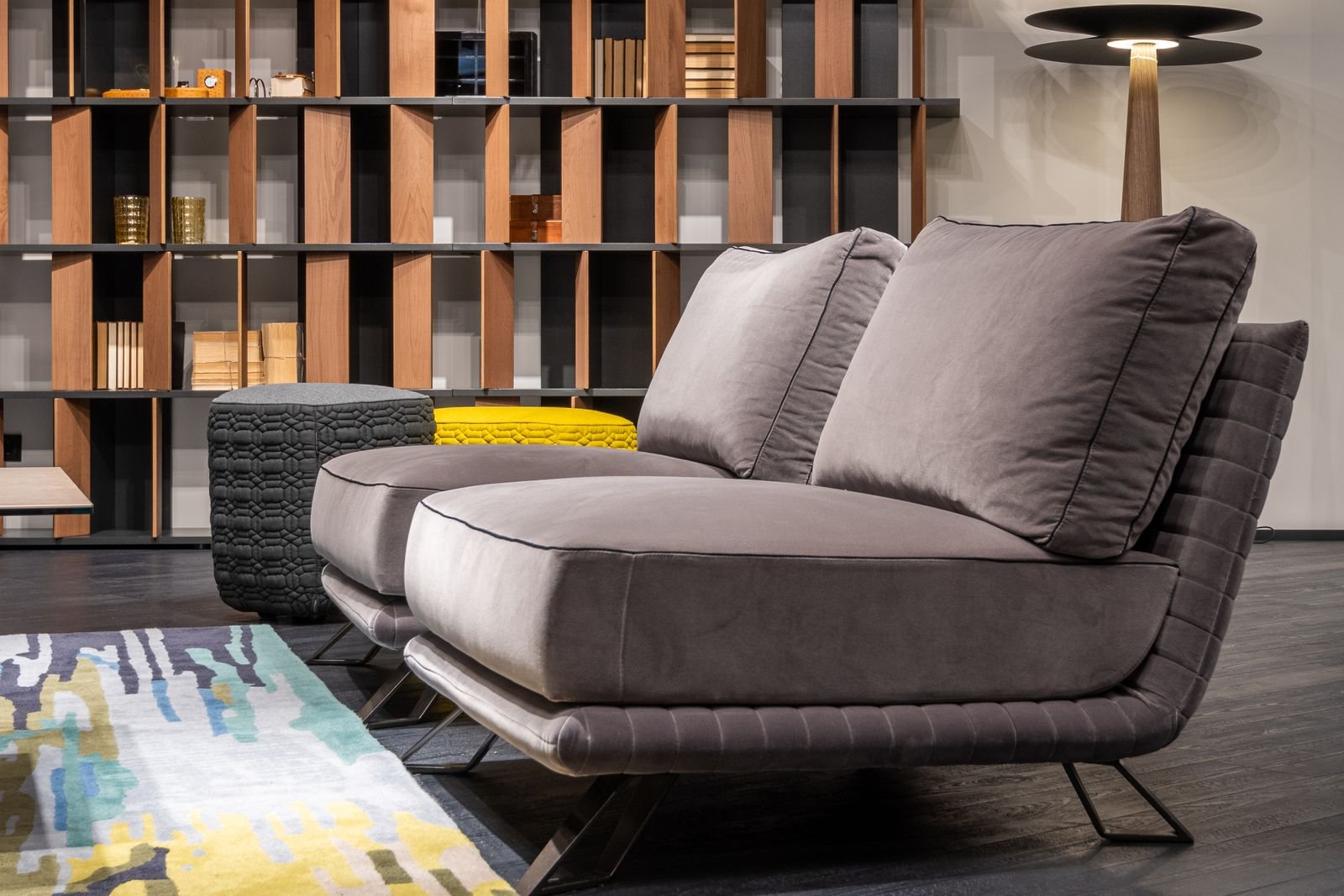 Living room with a settee, poufs, bookcase and lit lamp.