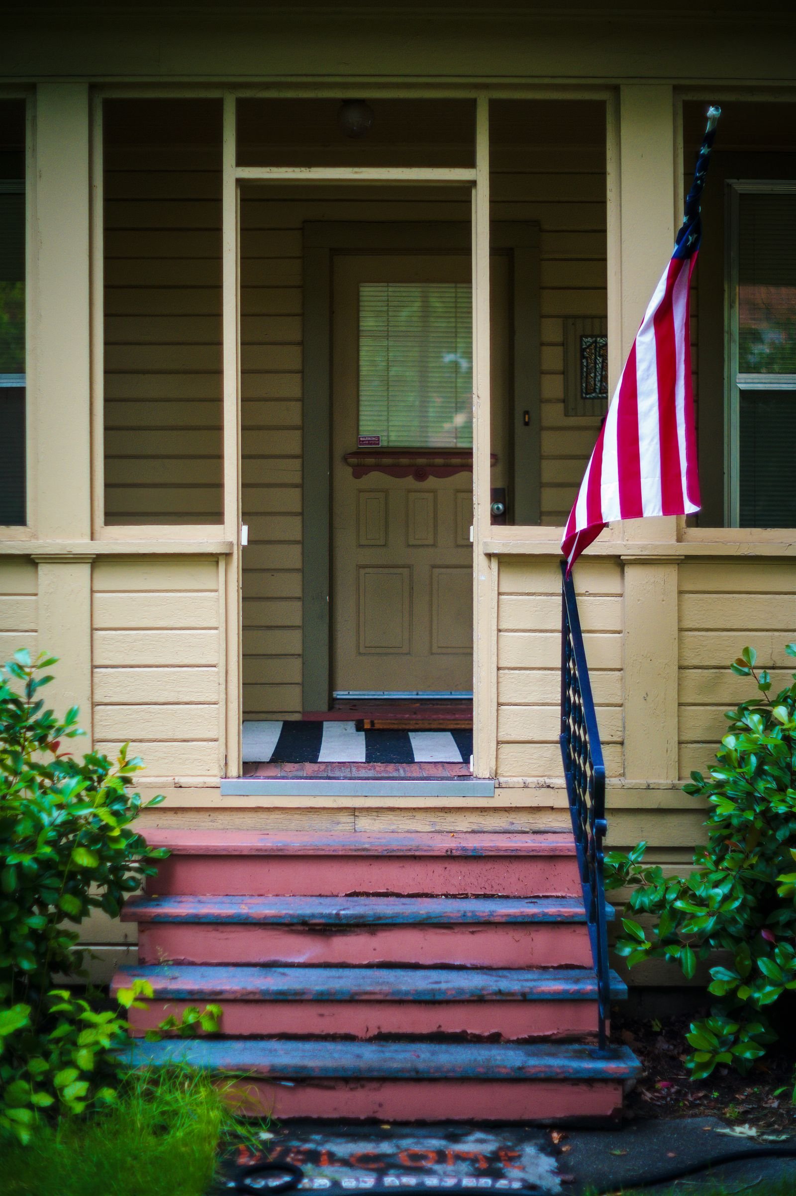 House entrance with steps, greenery and an American flag.