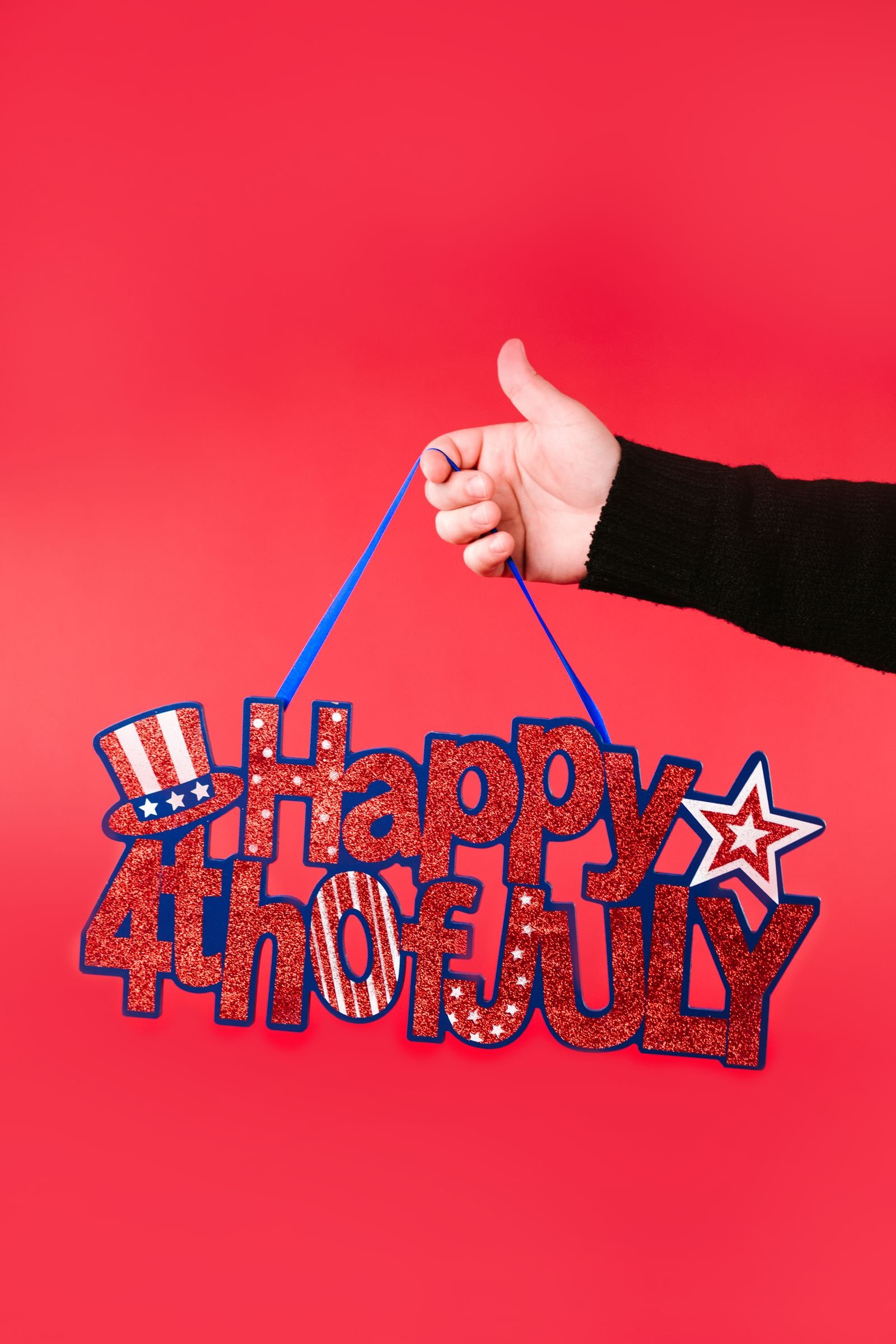 Glittery Happy 4th of July sign hanging against a red backdrop.