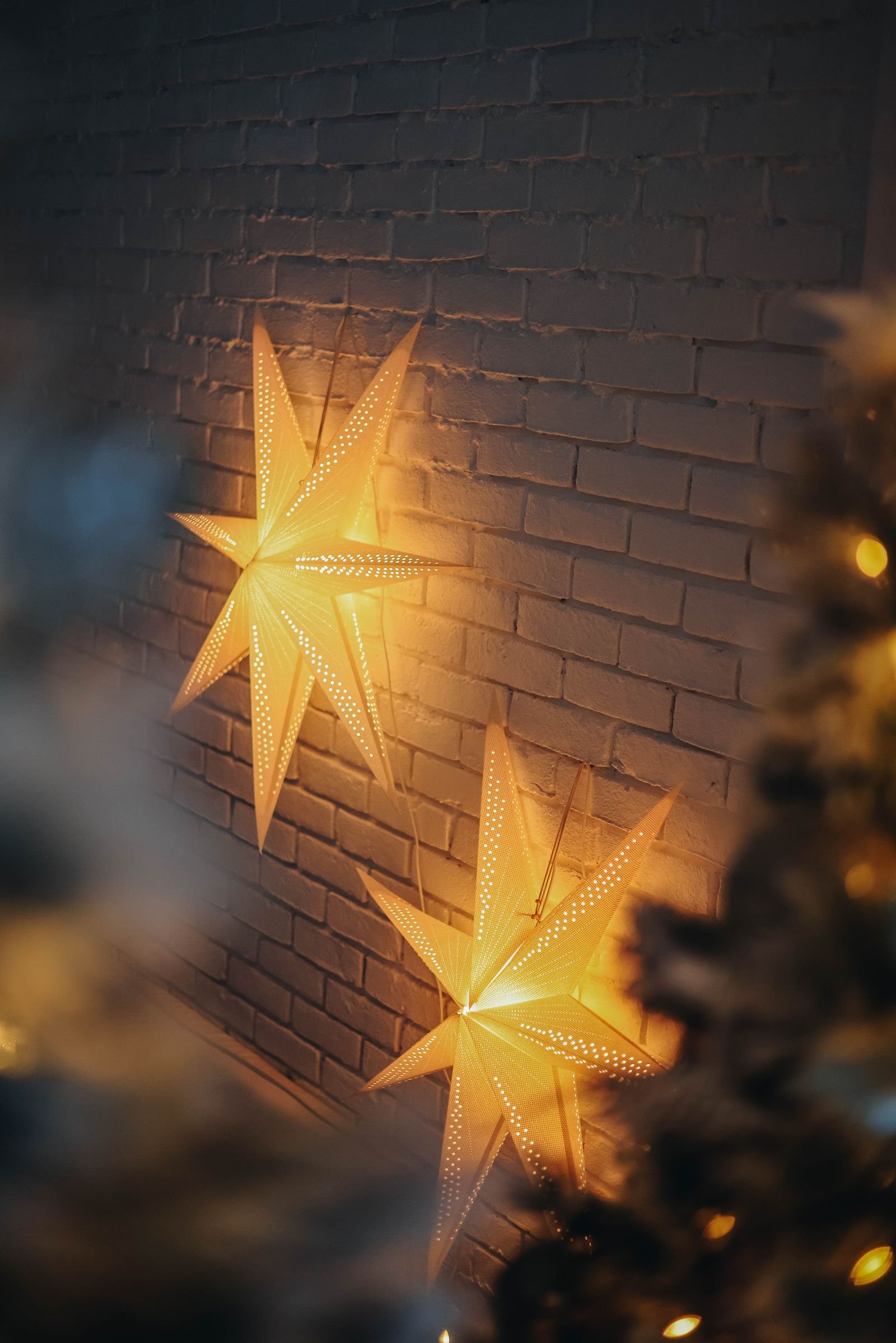Illuminated paper stars hanging on a white brick wall.