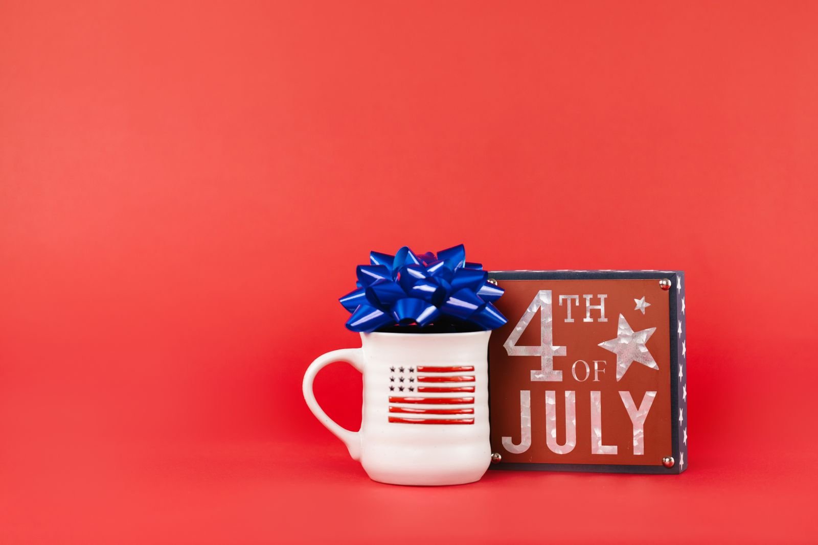 4th of July mug and sign with a blue ribbon on a red background.