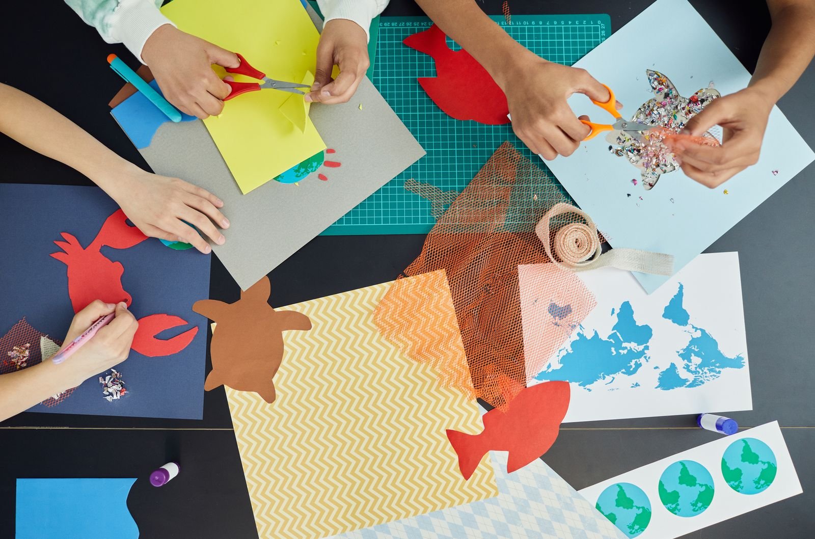 Top view of children making colorful paper crafts at a table.