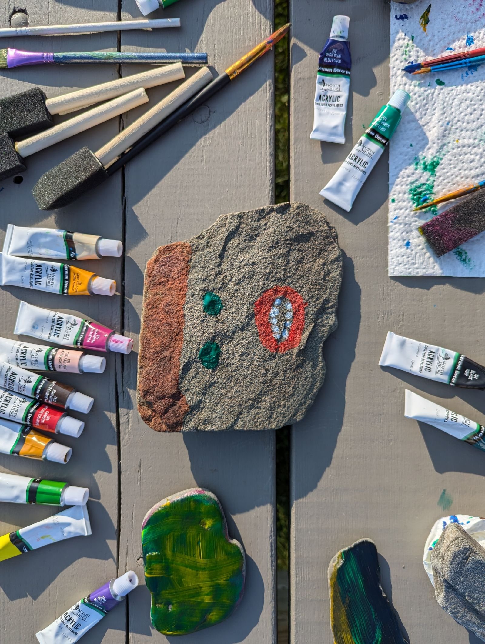 Painted rock with acrylic paints and brushes on a wooden table.