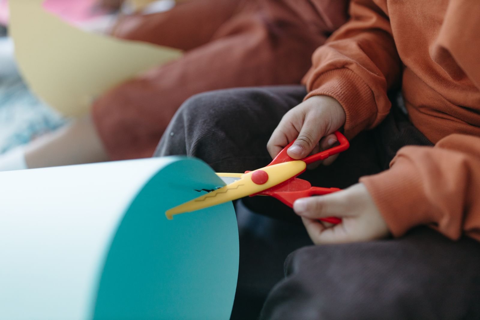 Child's hands cutting paper with colorful scissors.