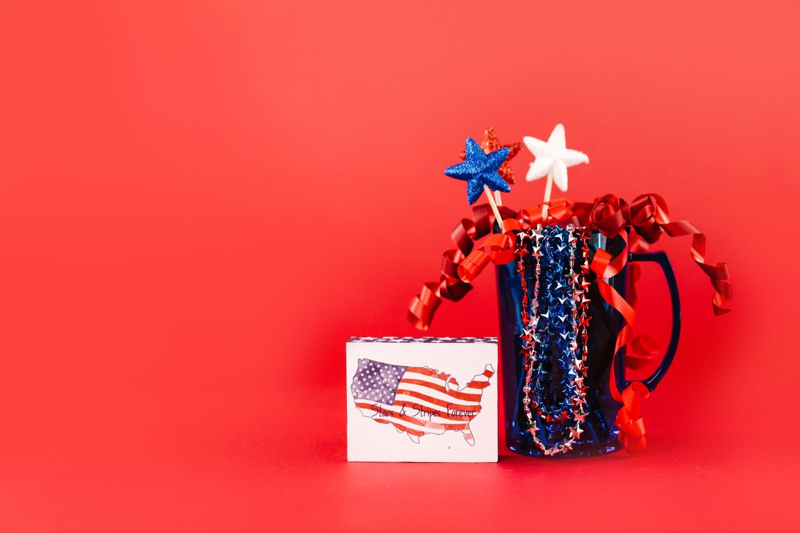 Red, white and blue Fourth of July decorations on a red background.