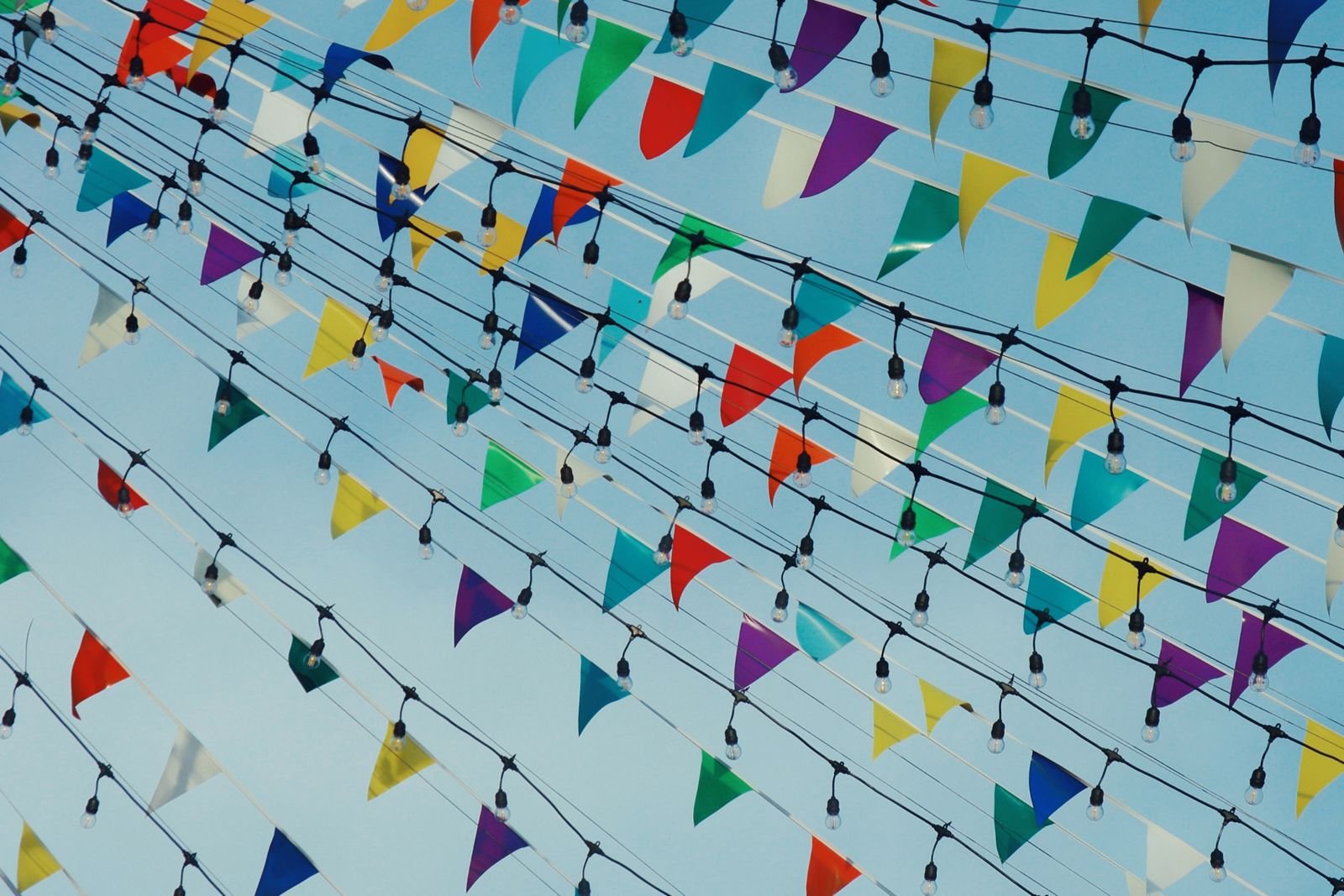 Colorful festival bunting and string lights hanging against a clear blue sky.