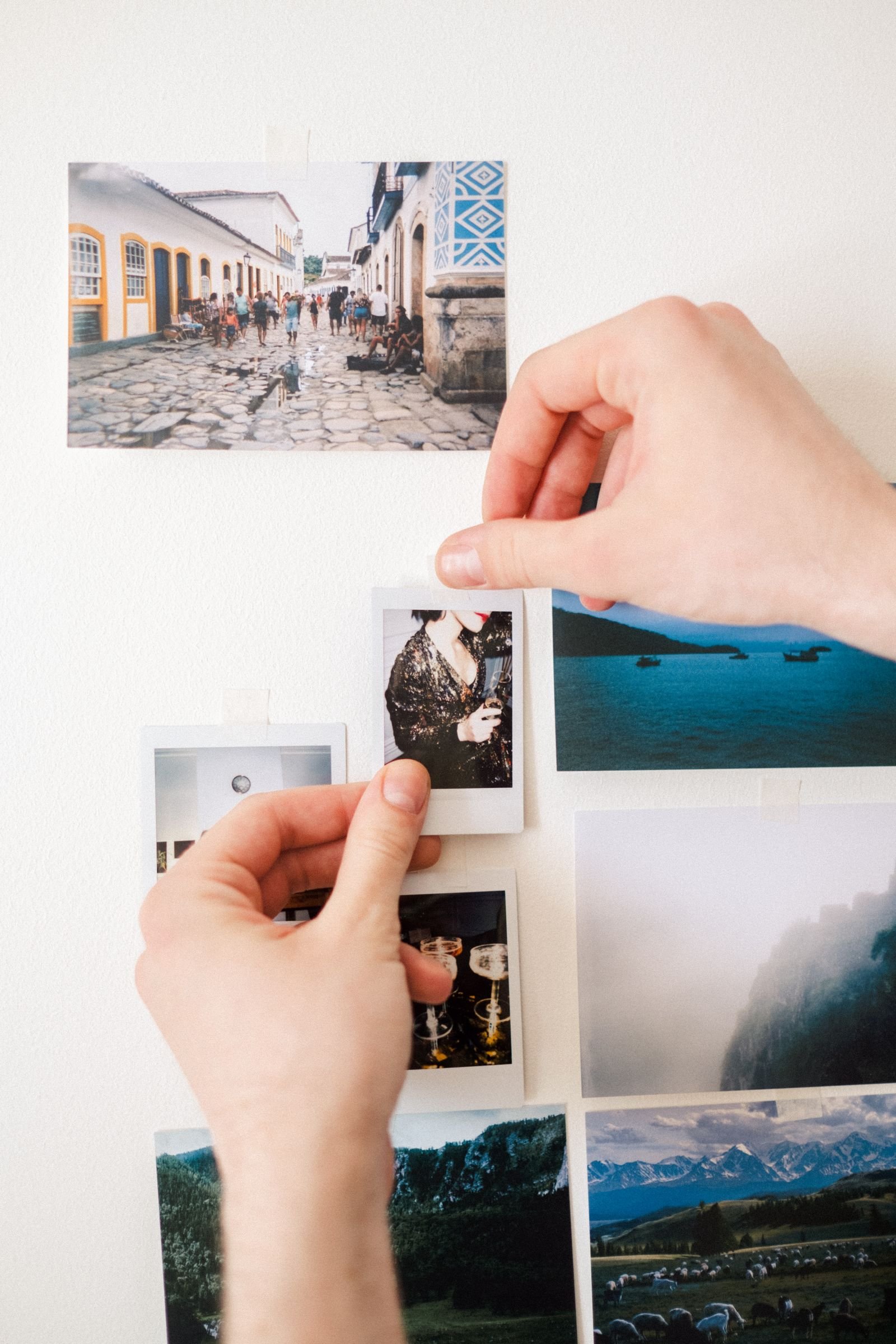Hands arranging a collage of photos on a plain white wall.