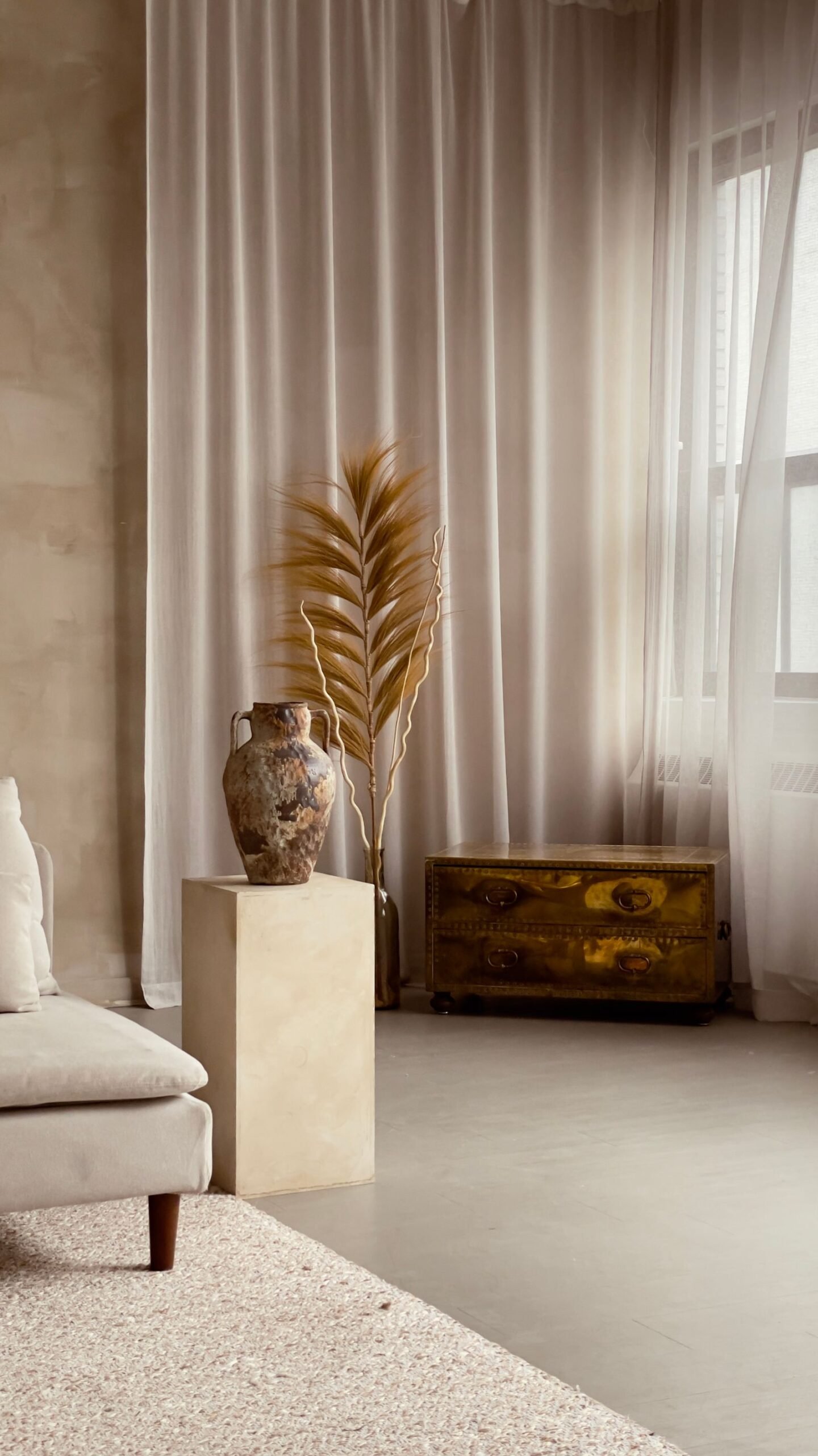 Neutral room with tall curtains, a metal vase and soft light.