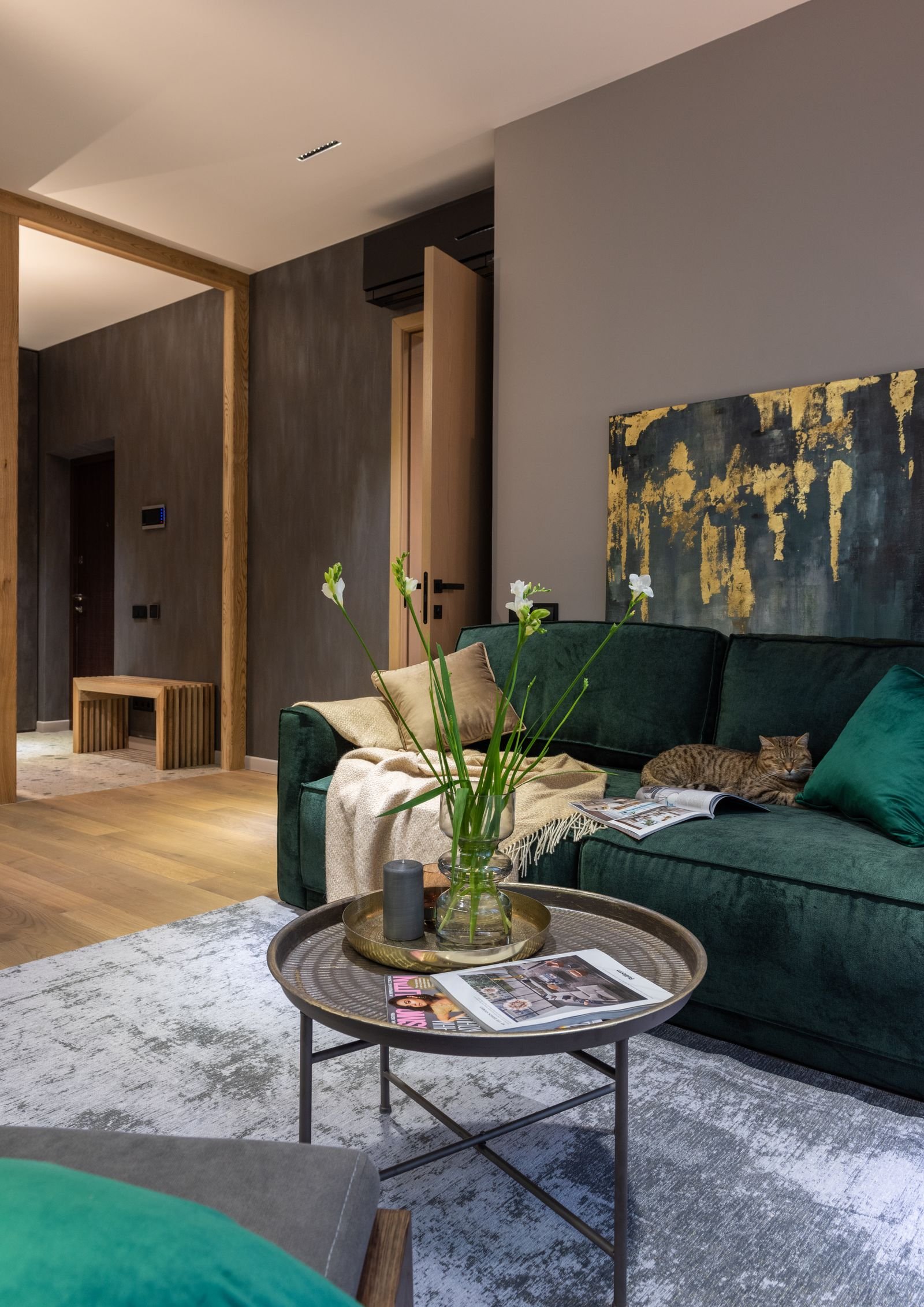 Green sofa with cushions beside a round coffee table with flowers.
