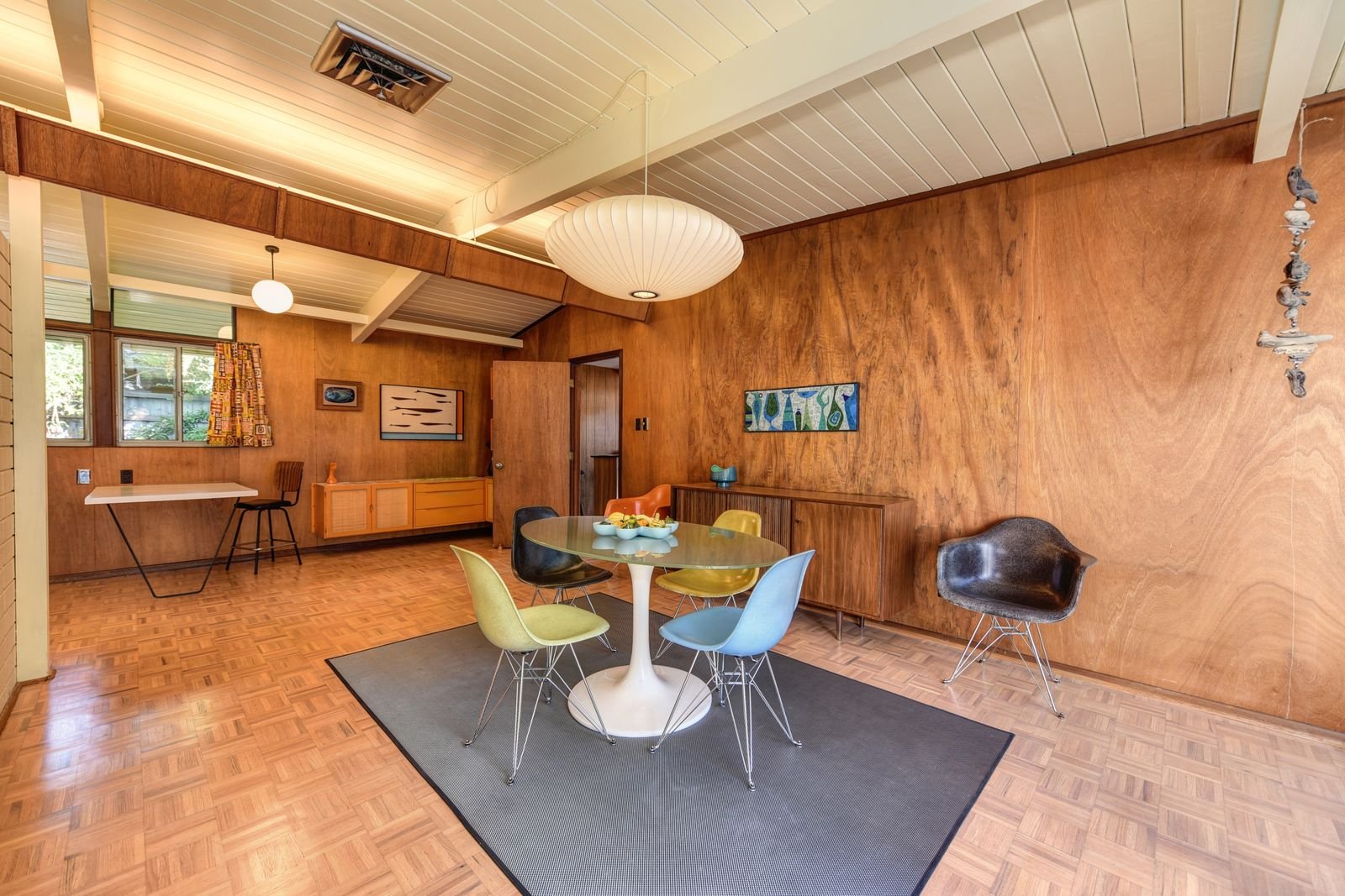 Mid-century dining room with colorful chairs and wood paneling.