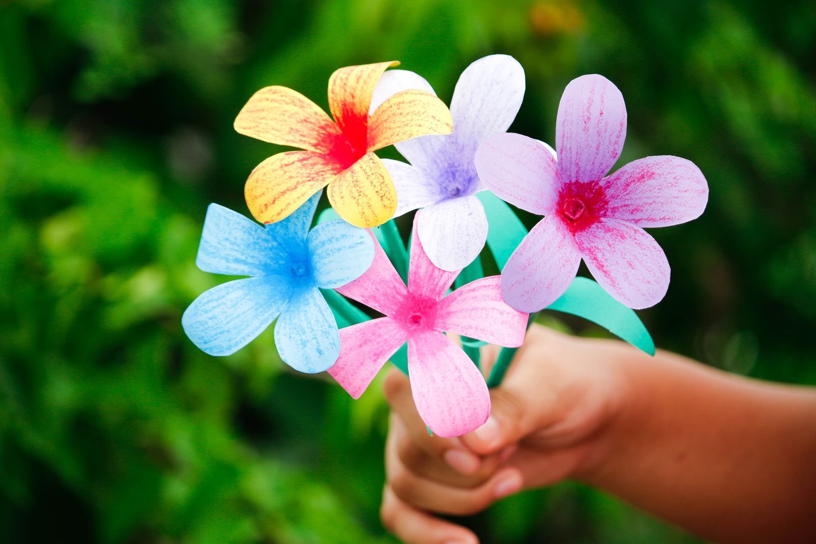 Hand holding a bunch of colorful handmade paper flowers.