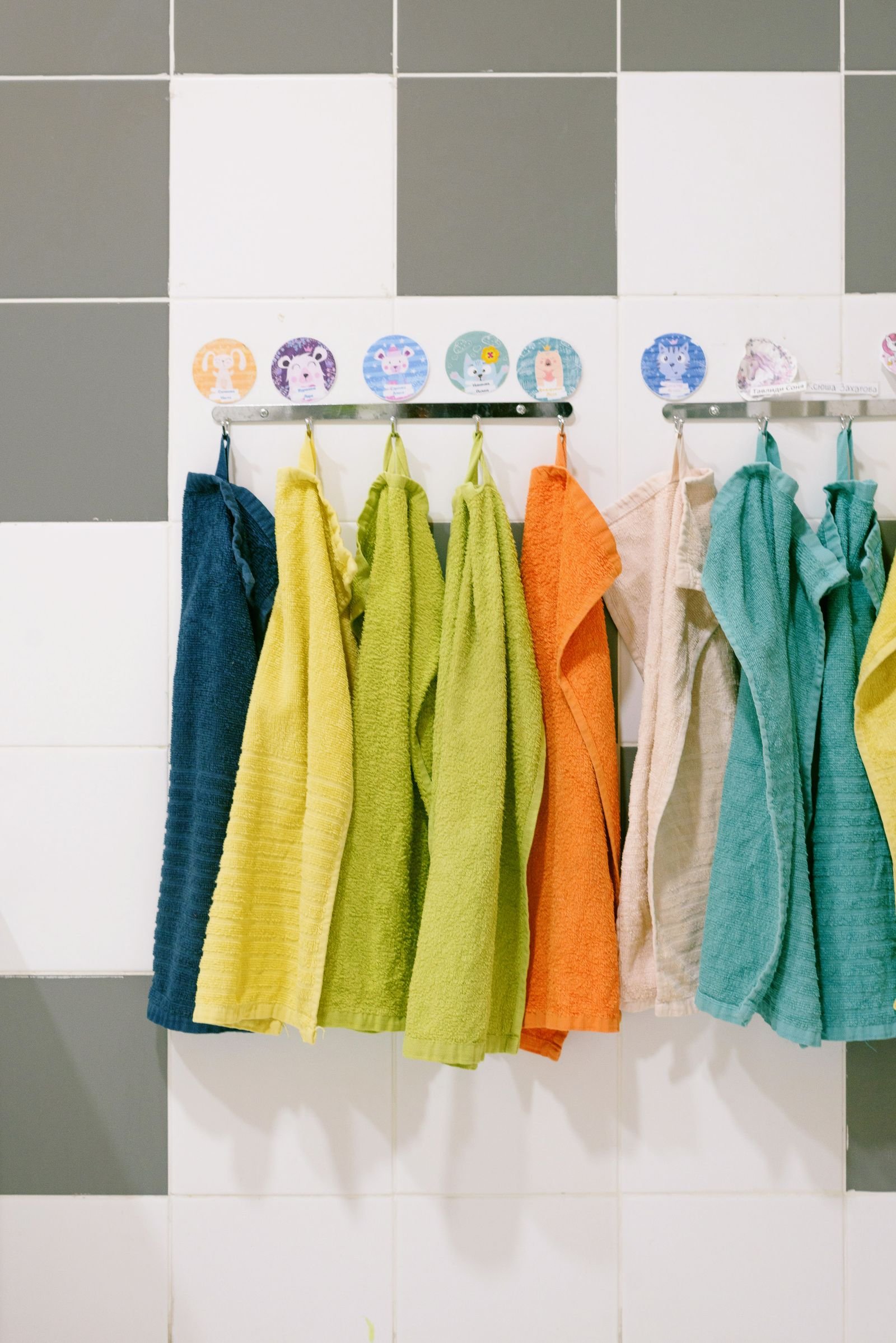 Colorful bath towels hanging on a rack against a tiled wall.