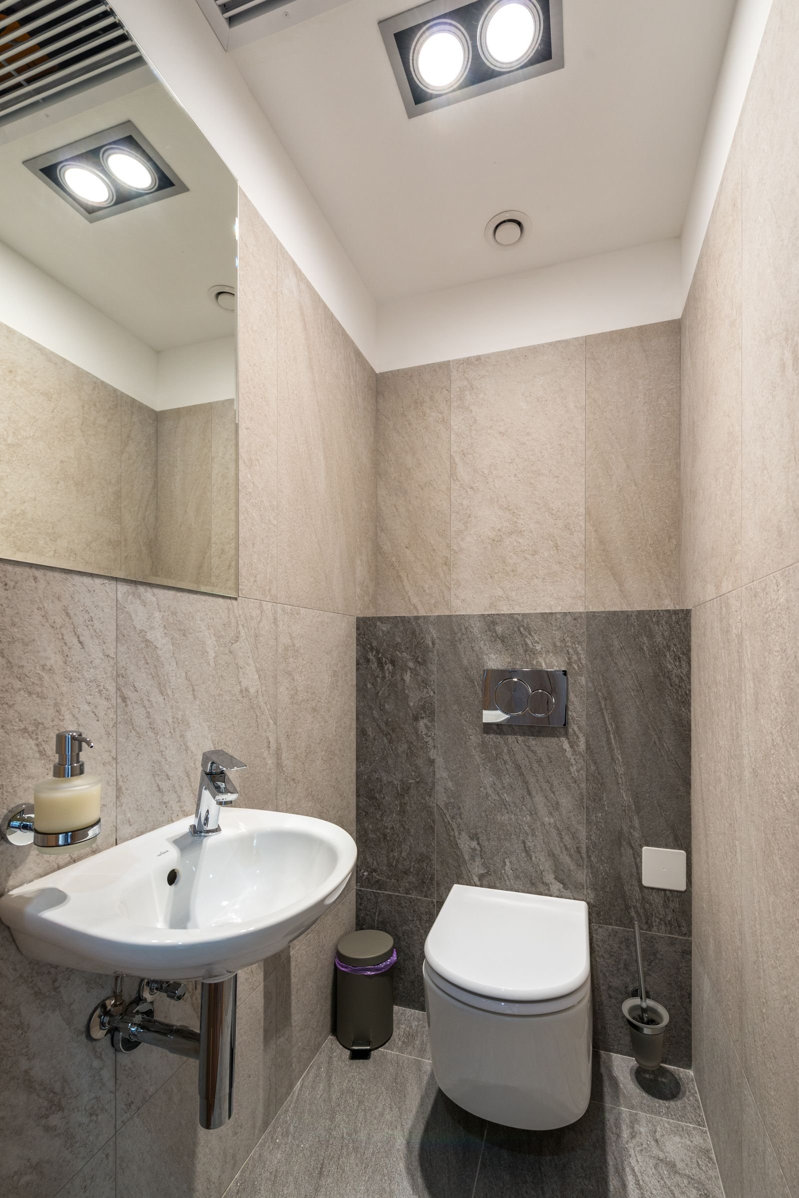 Tiled bathroom with a white ceramic sink, toilet and mirror.