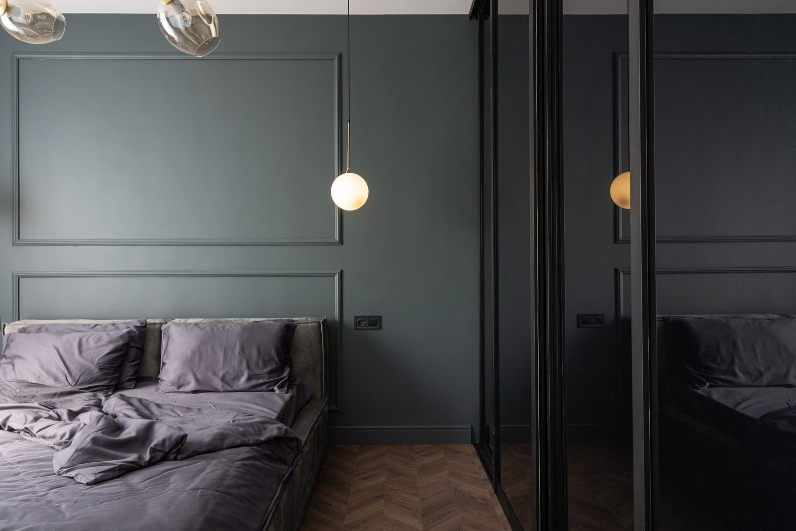 Modern bedroom with gray bedding and a lamp hanging over the bed.