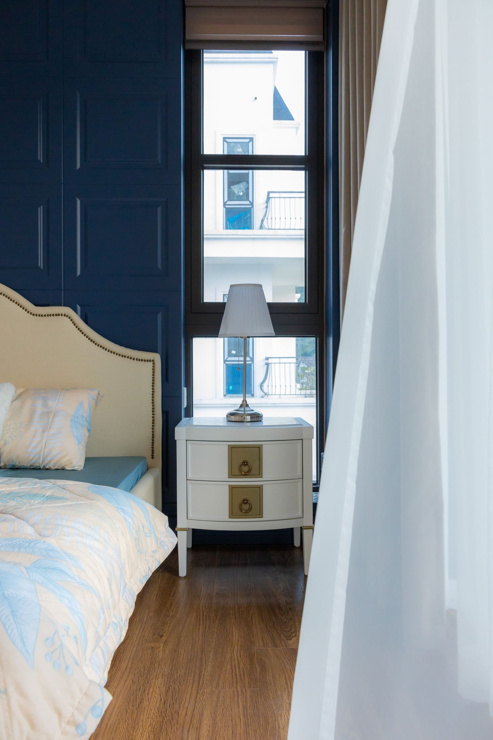 Bedroom with a beige headboard, blue walls and wood flooring in natural light.