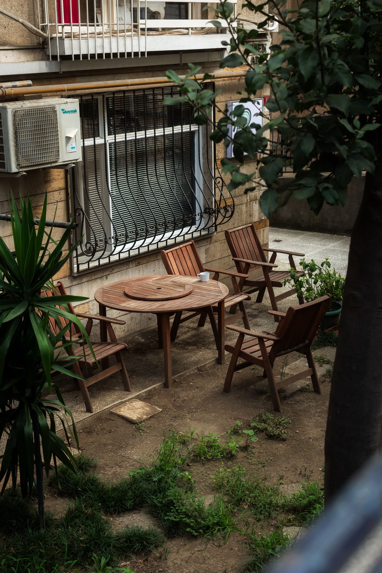 Backyard patio with wooden chairs and a round table among greenery.