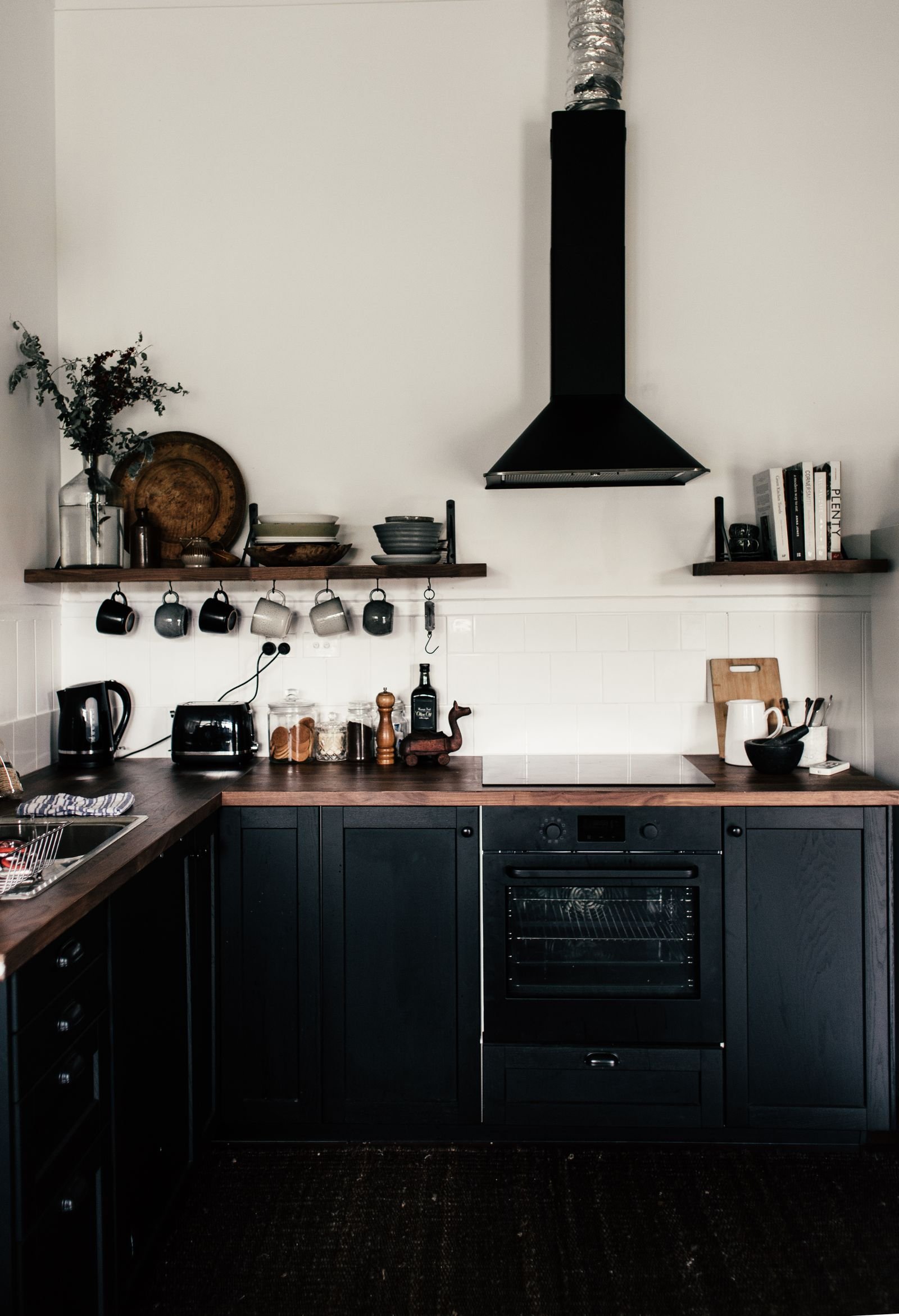 Contemporary kitchen with black wooden cupboards and open shelves of utensils.