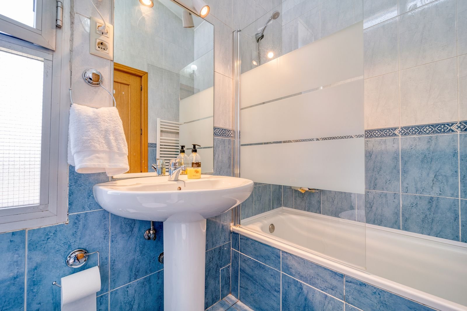 Minimalist bathroom with blue tiles, a glass shower and a white sink.