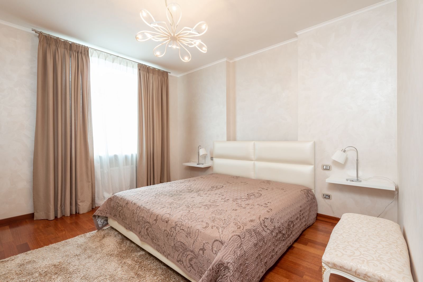 Classic bedroom with a comfortable bed, a bench, a chandelier and lamps.