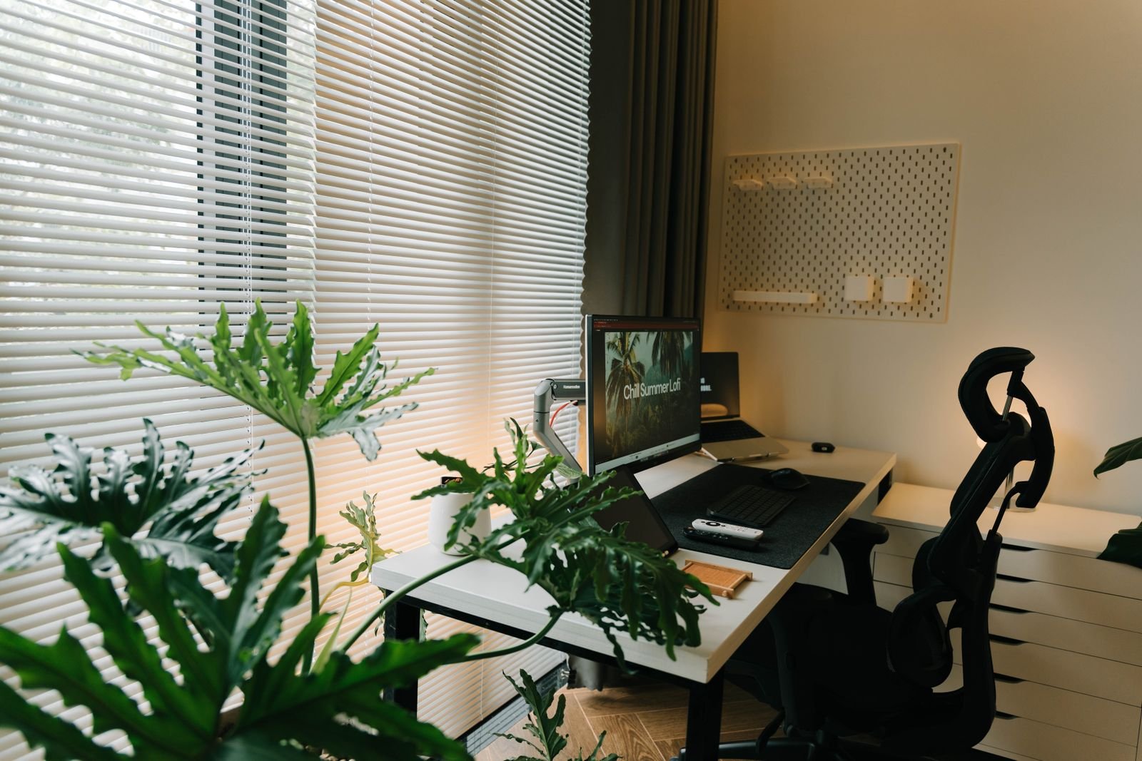 Home office with a desk, chair and green plants beside a window.