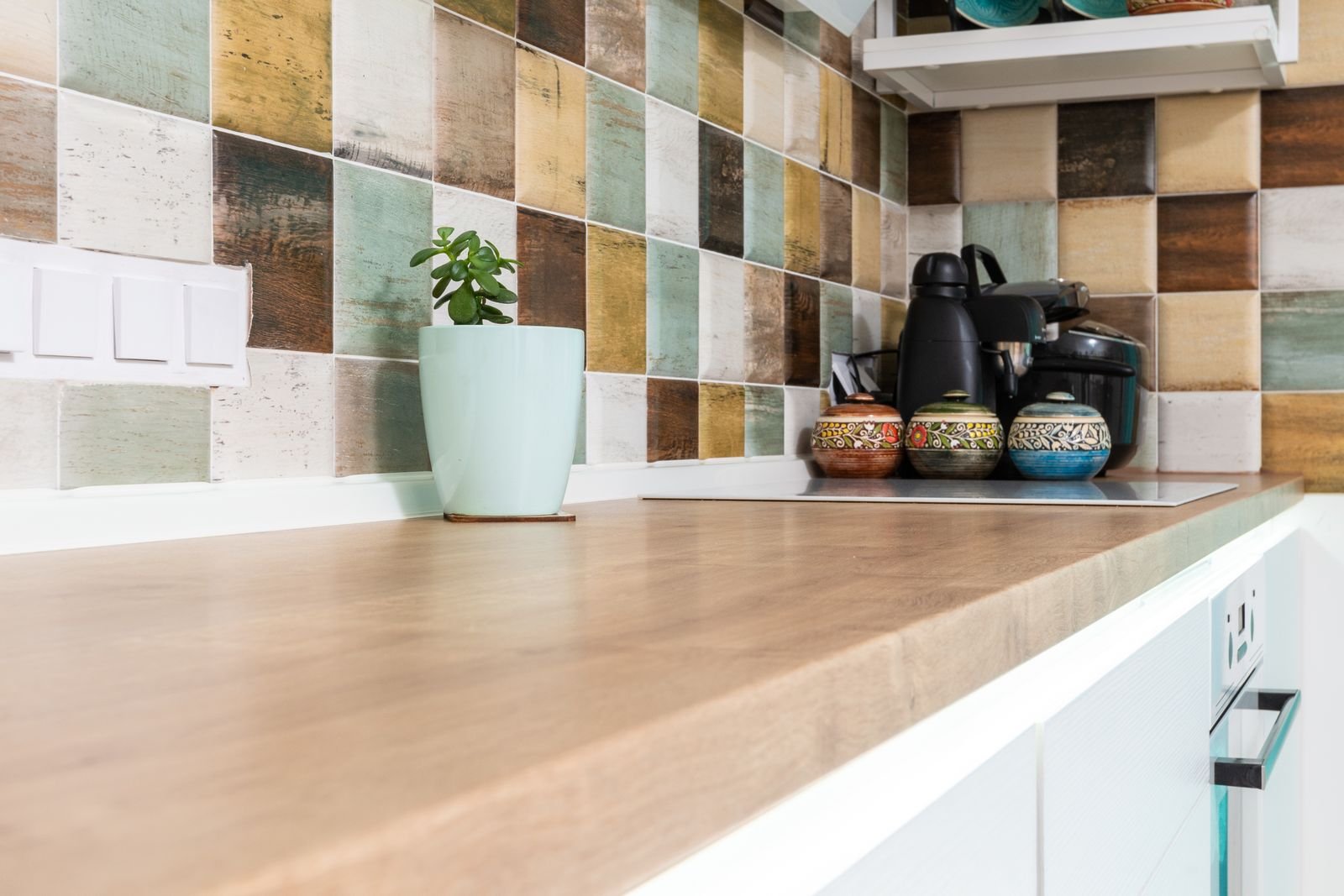 Light kitchen corner with a multicolored tiled backsplash and dishware.